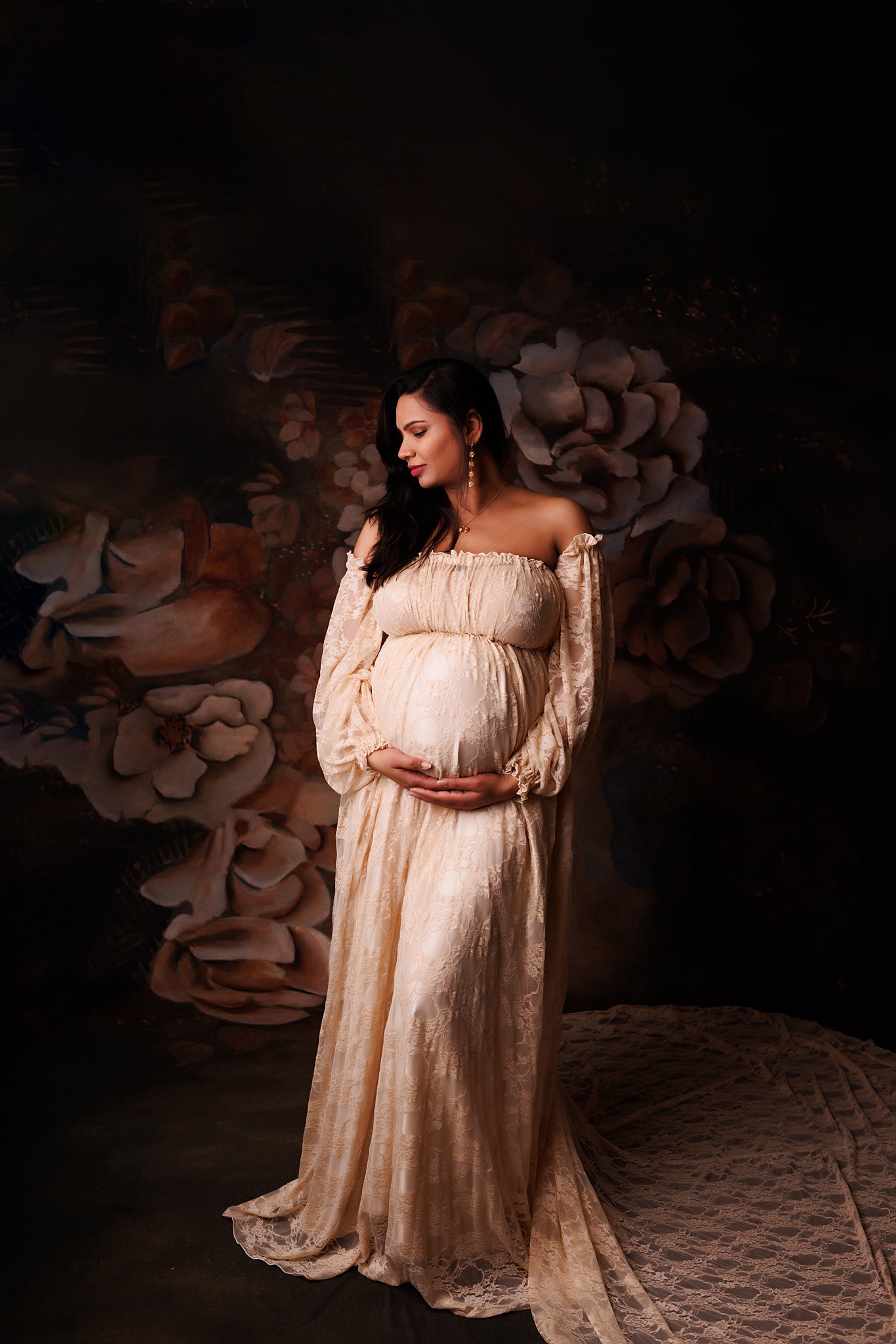 A mother to be wearing a white maternity gown with a long lace train stands in a studio 3d ultrasounds Toronto