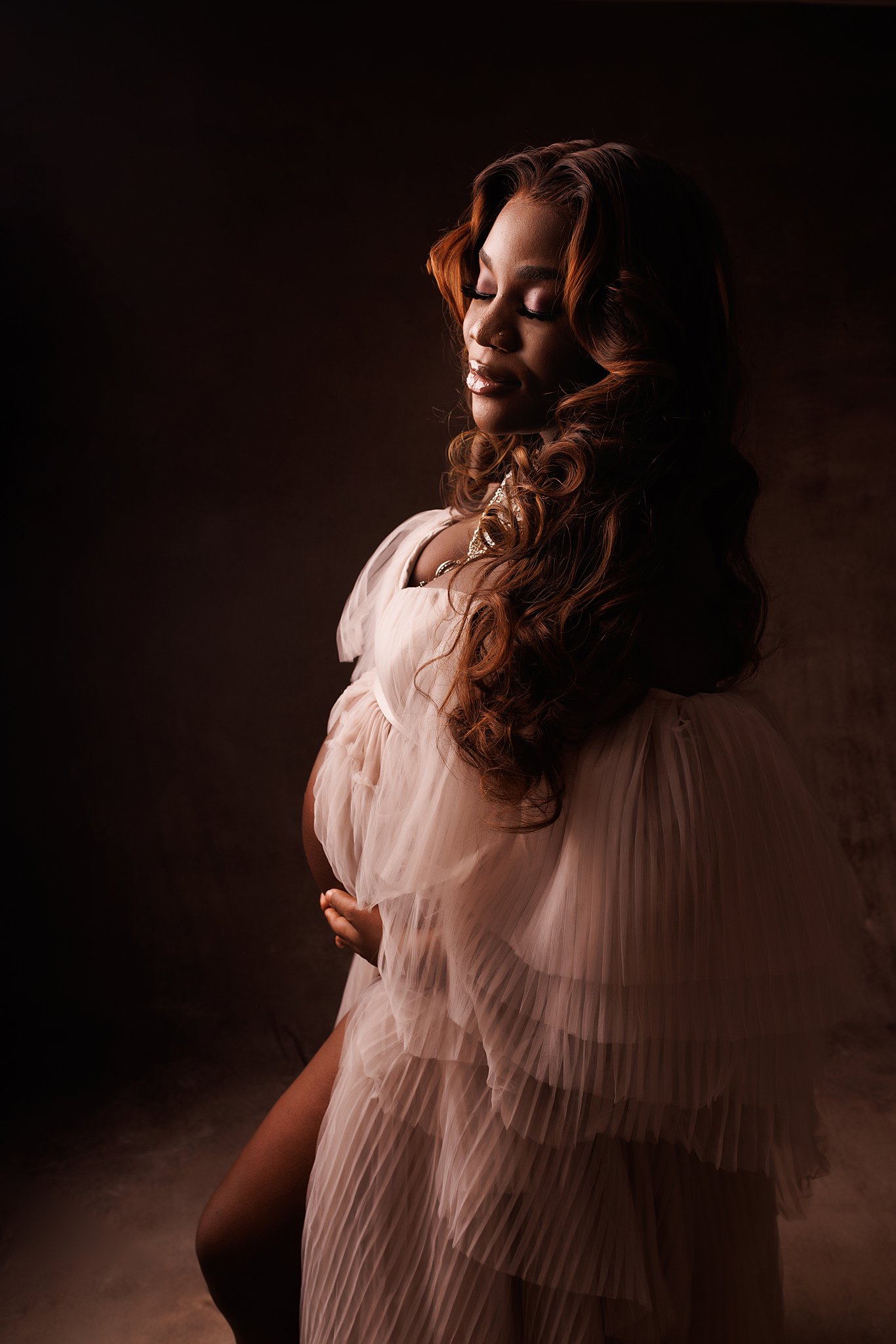A mother to be wearing a flowy maternity dress stands in a studio holding her bump Markham prenatal