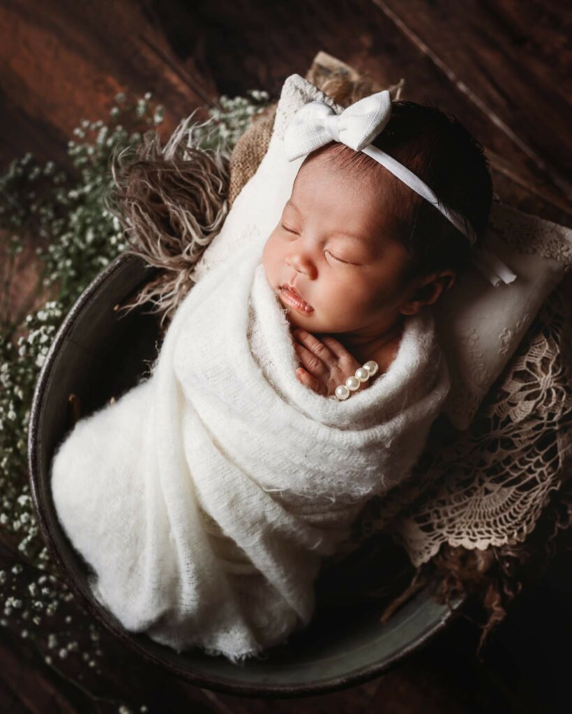Newborn baby girl in a bucket wrapped in cream with a cream bow - Barrie Newborn Photography