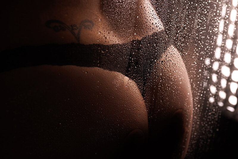 Woman's bum, in a black thong in the shower with water droplets on the glass