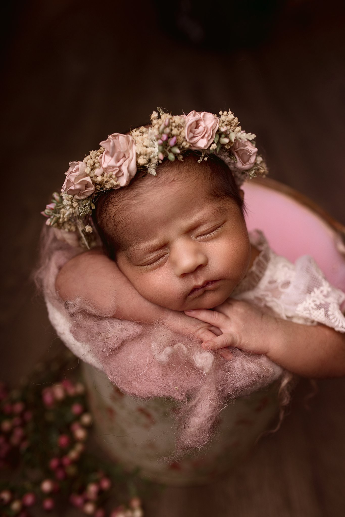 newborn baby wearing a floral headband sleeps in a large vase