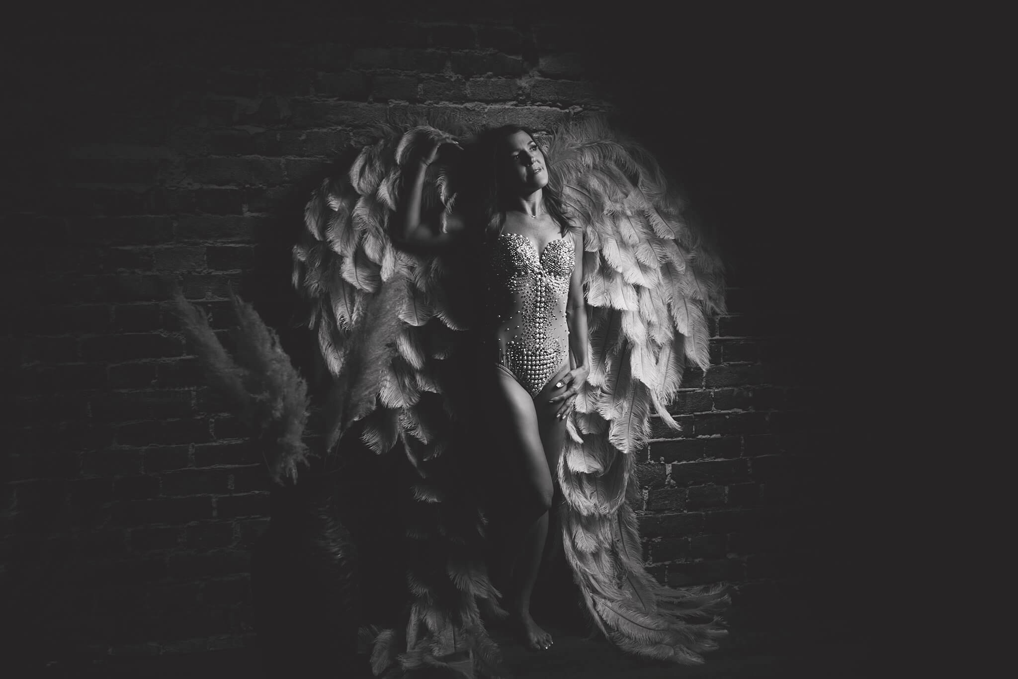 Photography by Toronto Photographer Shanna Parker Black and white image of a woman in a sparkly bodysuit and large feather wings leaning against a brick wall