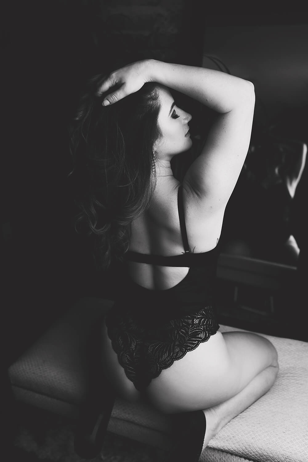 Black and white photo of a woman sitting with her back to the camera front of a mirror in black lingerie, hand in her hair Toronto Boudoir Photographer Shanna Parker