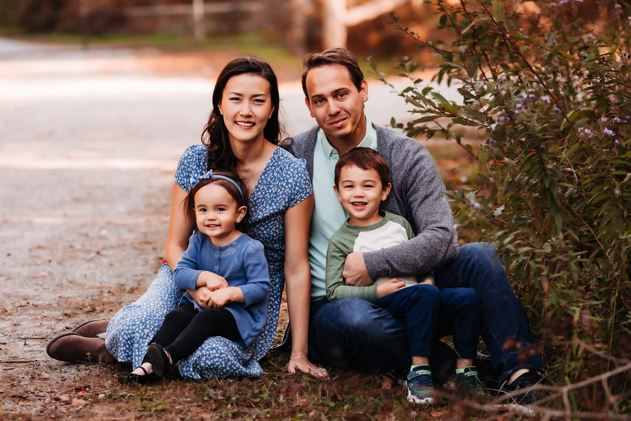 Family of four sit amongst fall colors posing for a family photo