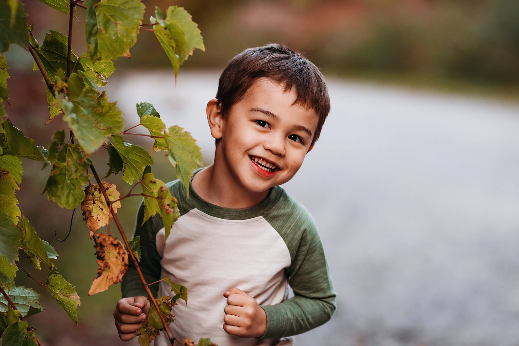 Little boy peeks out from behind some vines with a huge grin