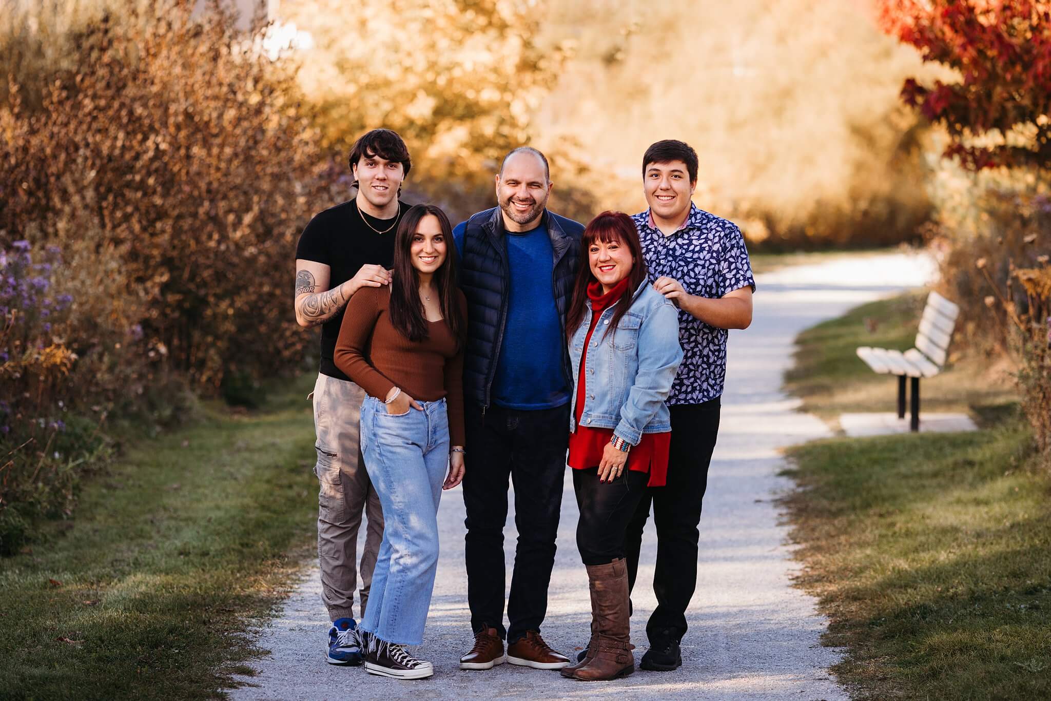 Family with 3 adult children stand posed together in the middle of a pathway