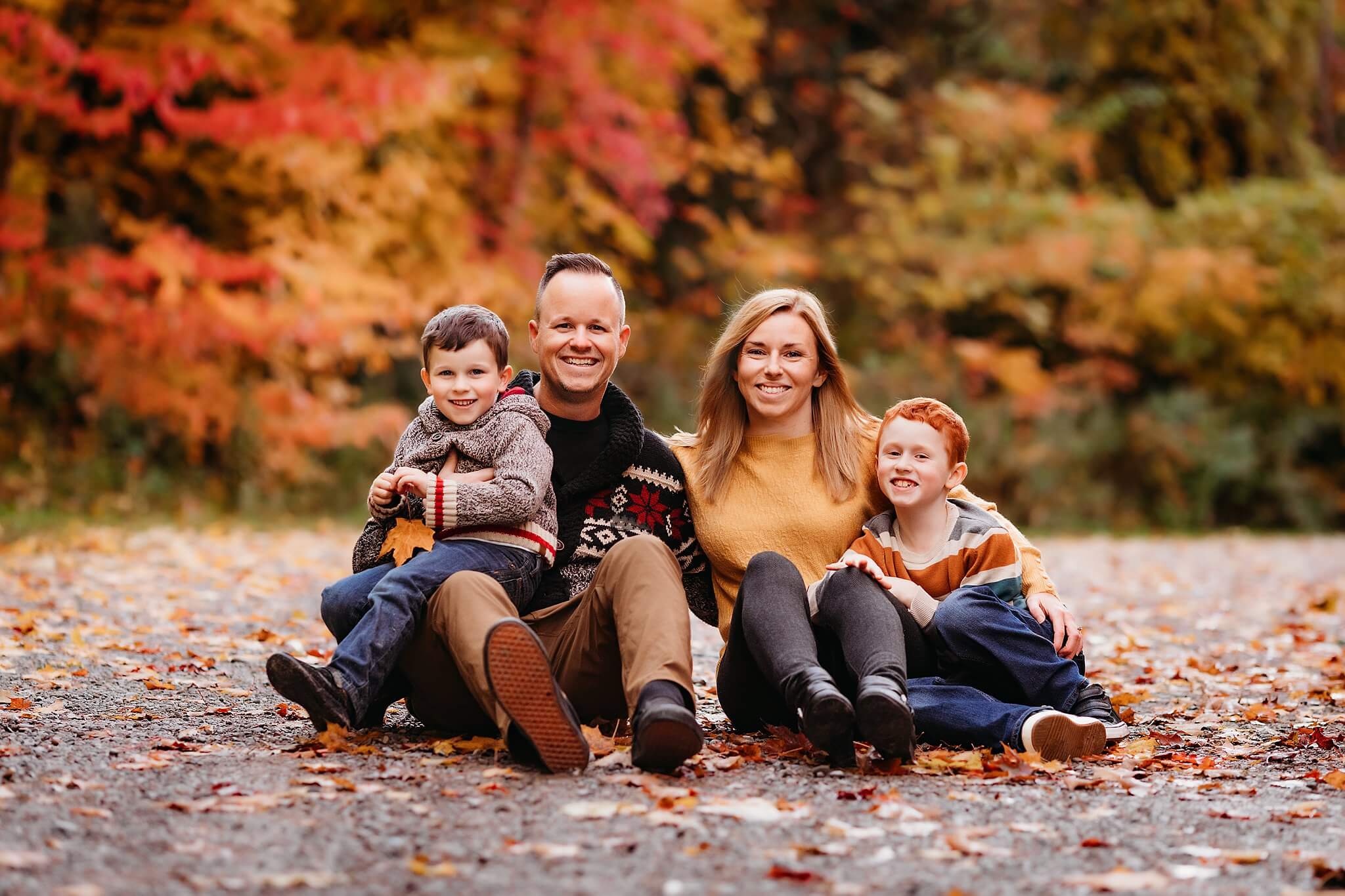 Family with two young boys sit amongst fall colors posing for a family photo