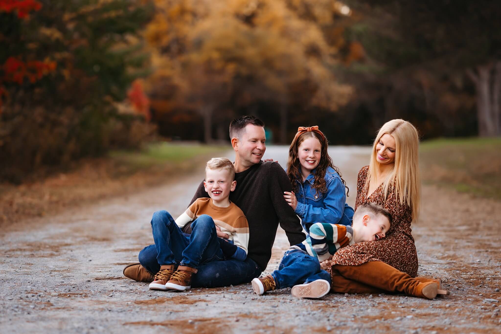 Family sitting together on a pathway in the fall, laughing and snuggling