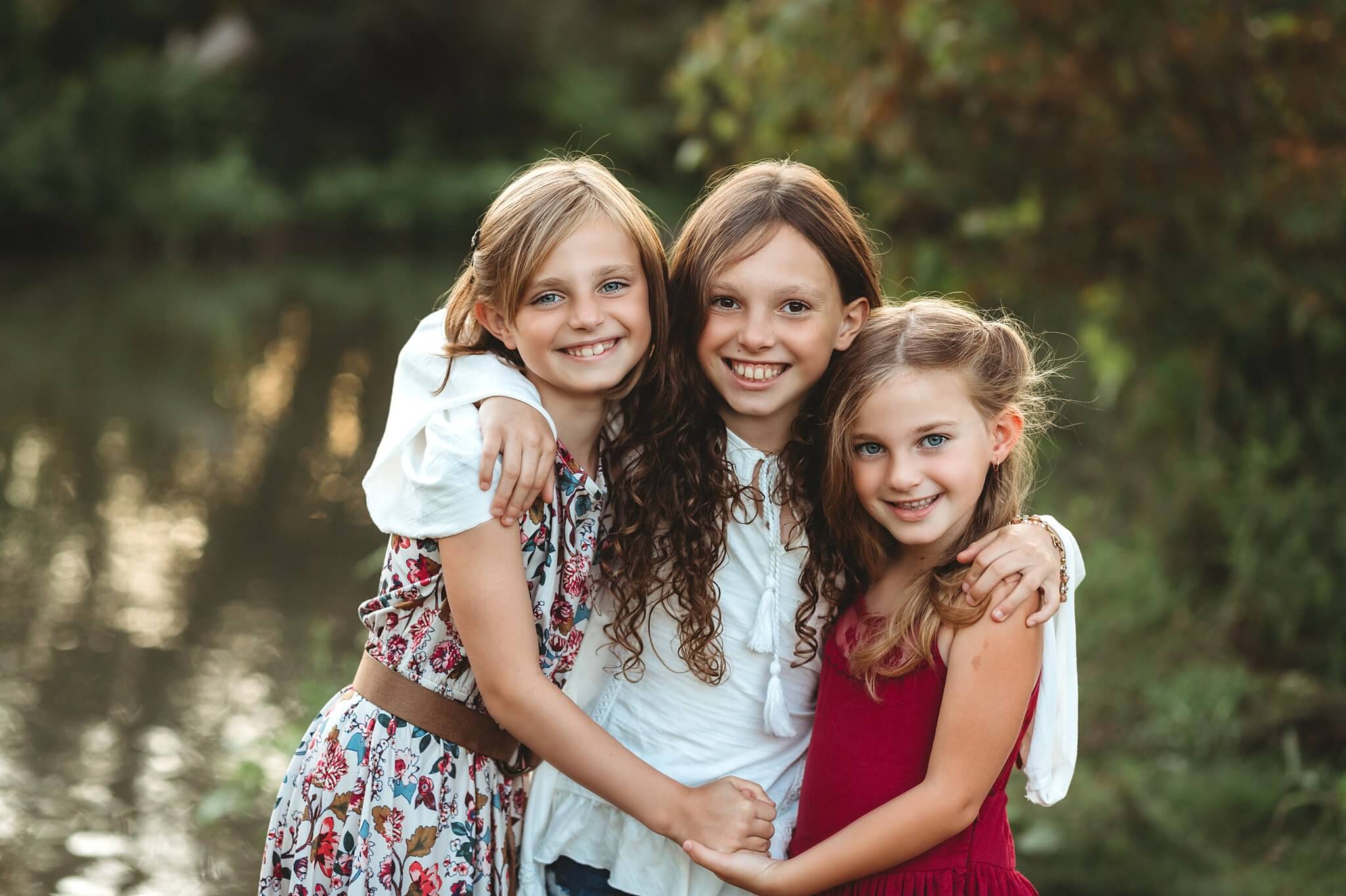 Three sisters embracing and smiling at the camera at sunset by Toronto Family Photographer