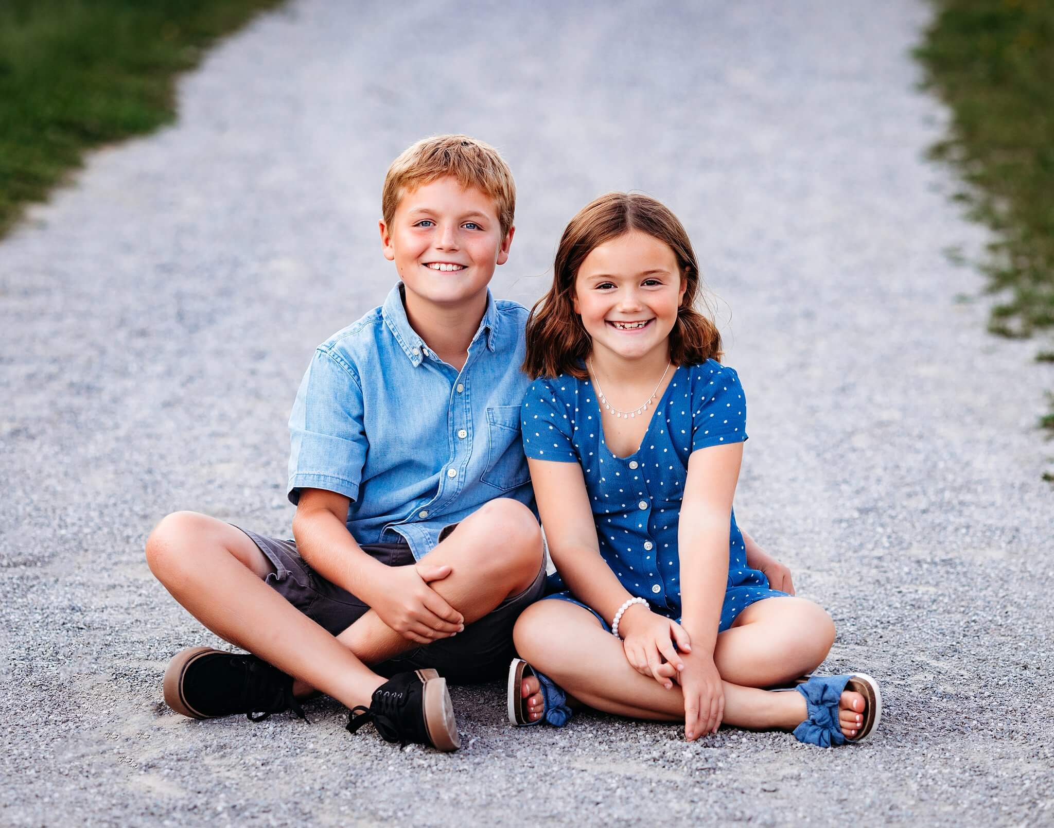 Brother and sister sitting on a pathway smiling at the camera