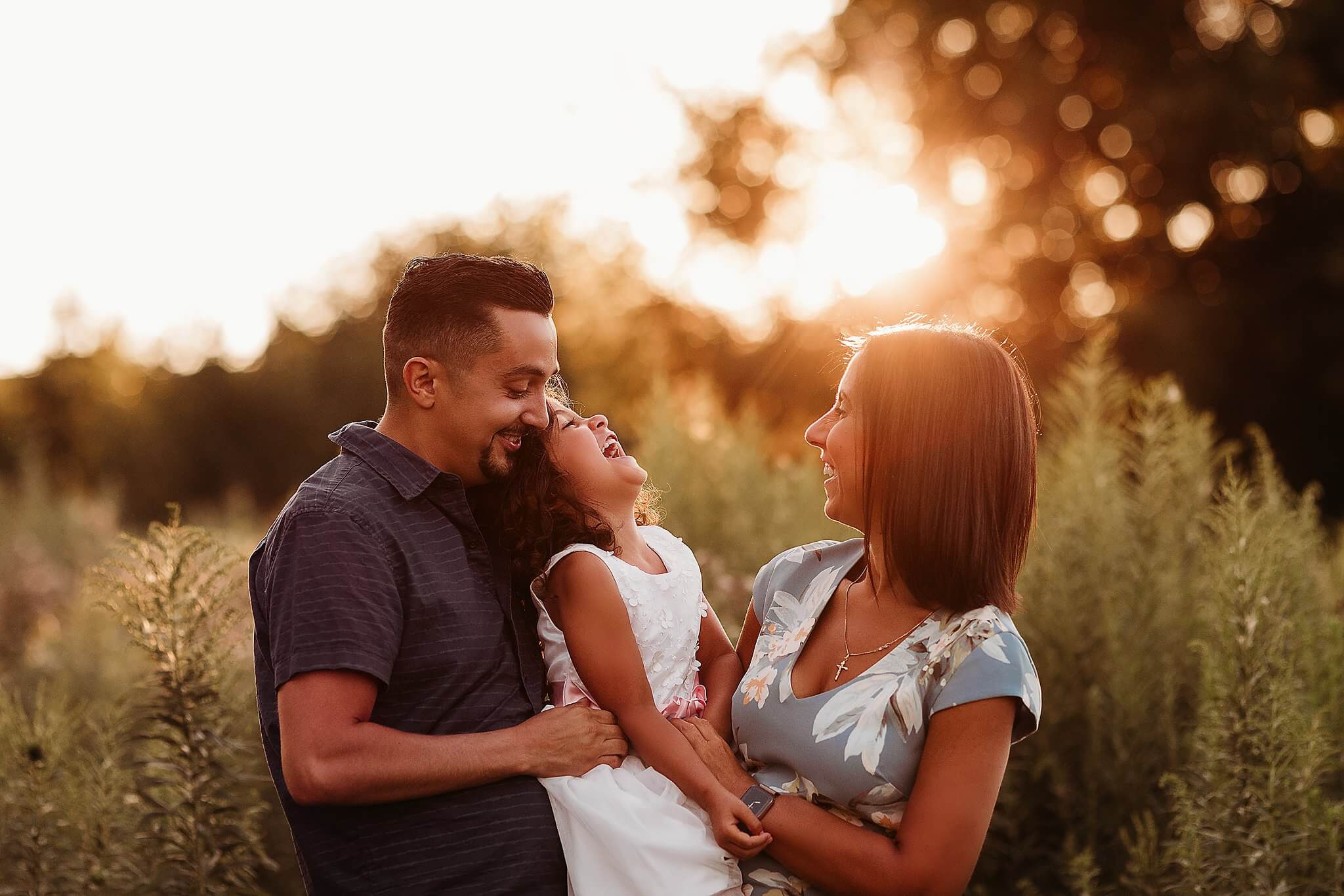 Photo of a Mother and Father holding and laughing with their daughter at sunset by Toronto Family Photographer