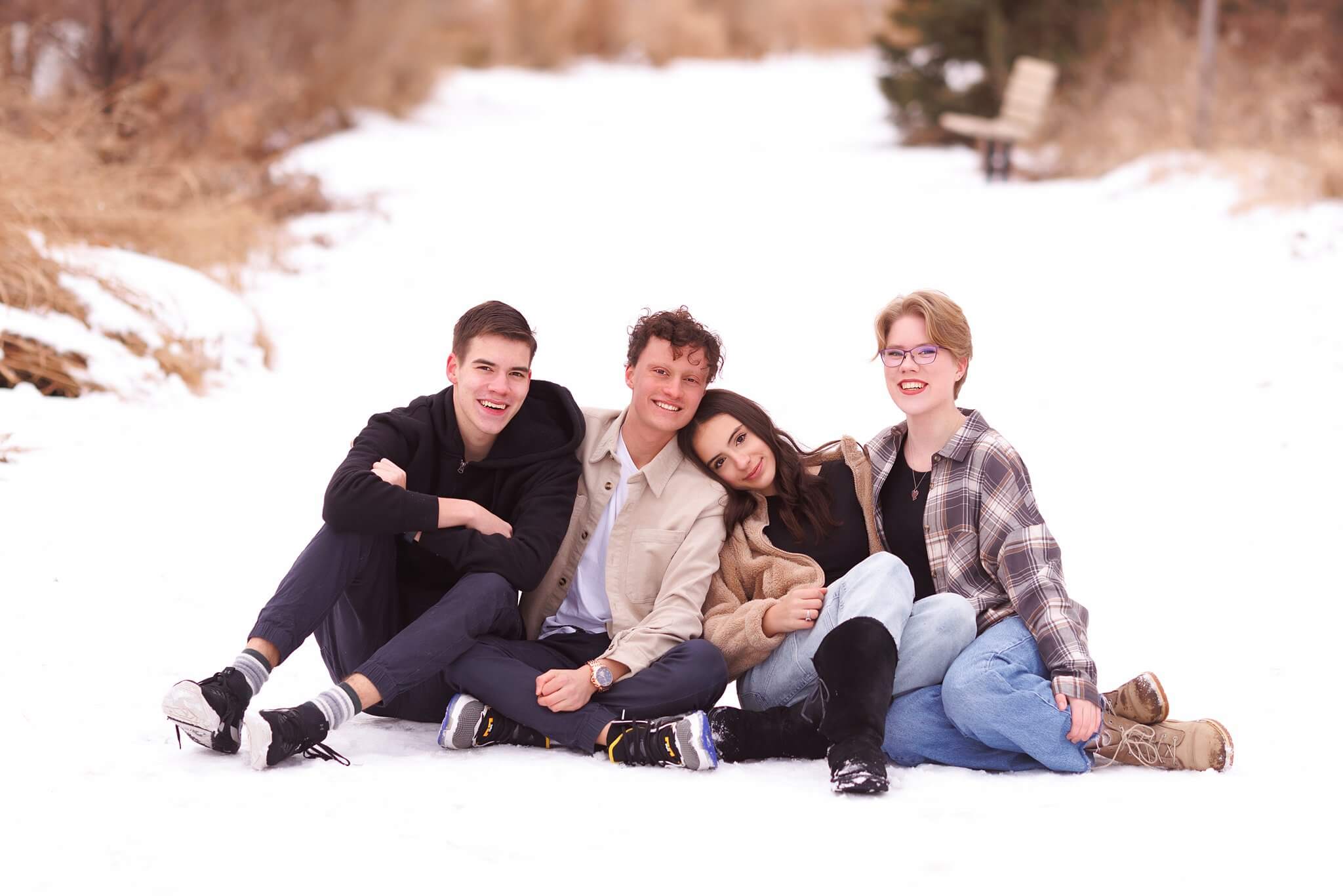 Winter photo of 4 teenage siblings sitting on a snow covered path