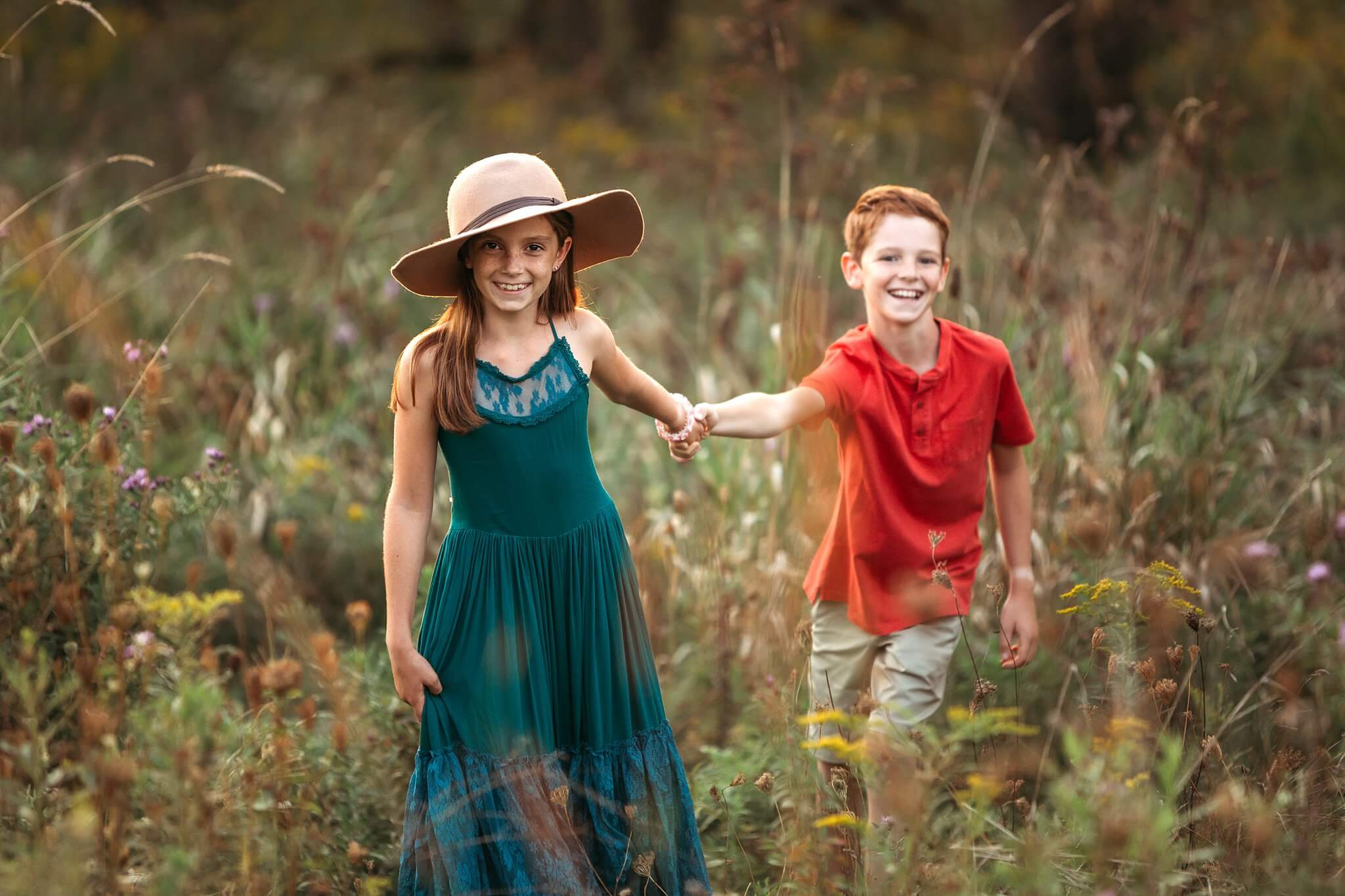 Stylish brother and sister holding hands and walking through tall grasses by Toronto Family Photographer