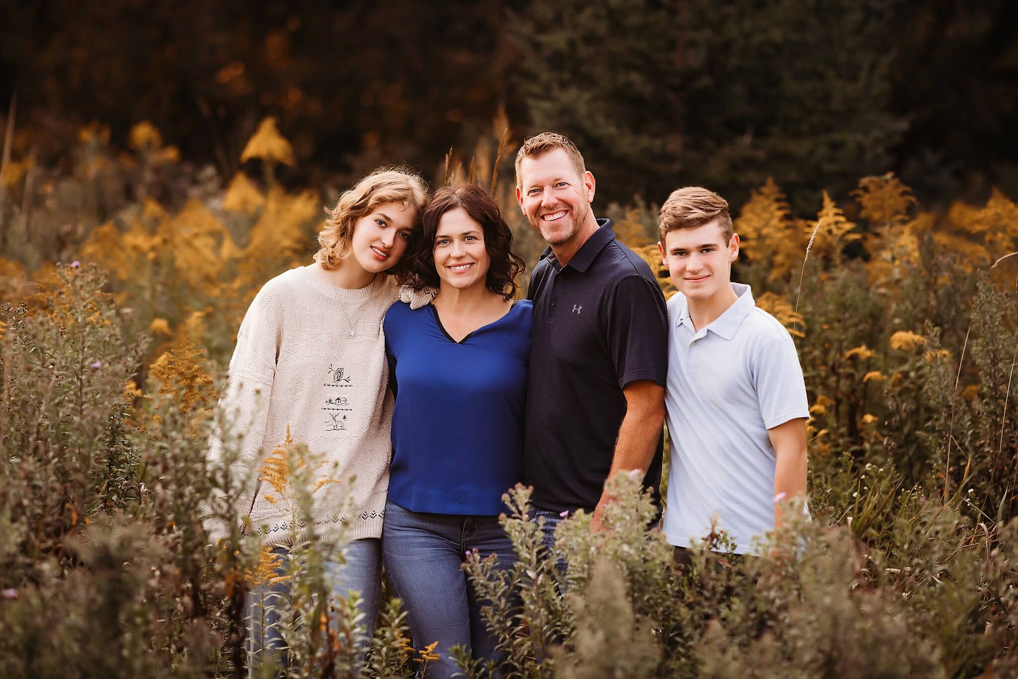 Family with a teenage son and daughter stand in tall wildflowers at sunset