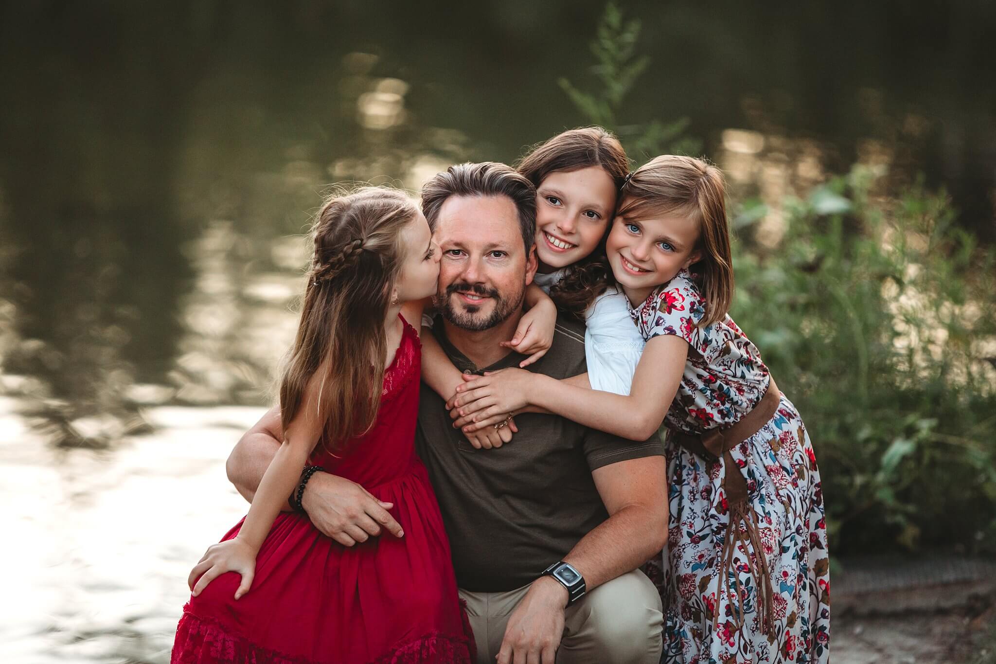 A father surrounded by his three young daughters with the setting sun on the water behind them