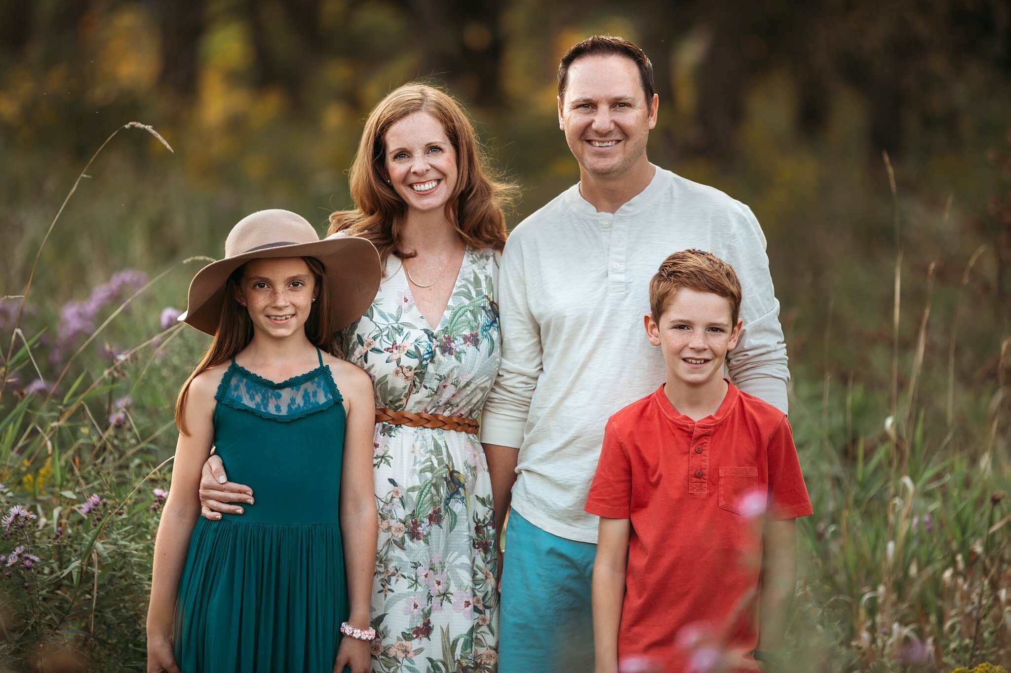 Family with son and daughter stand in tall grasses posing for a photo