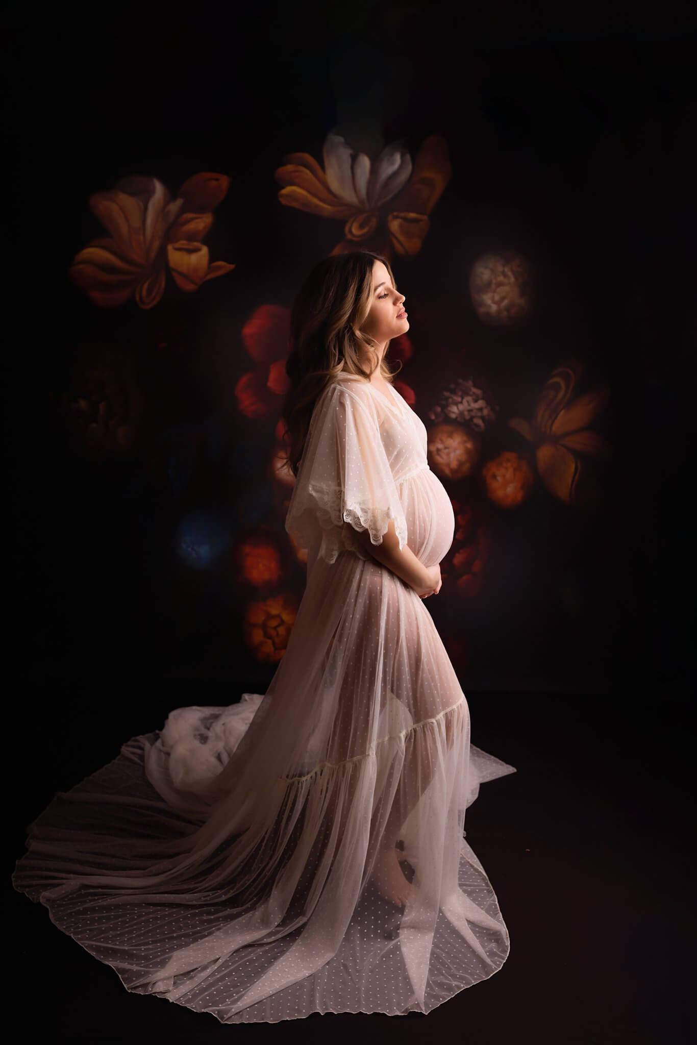 Pregnant Woman in an ivory sheer dress in front of a dark dramatic floral backdrop by Toronto Photography Maternity Photographer Shanna Parker