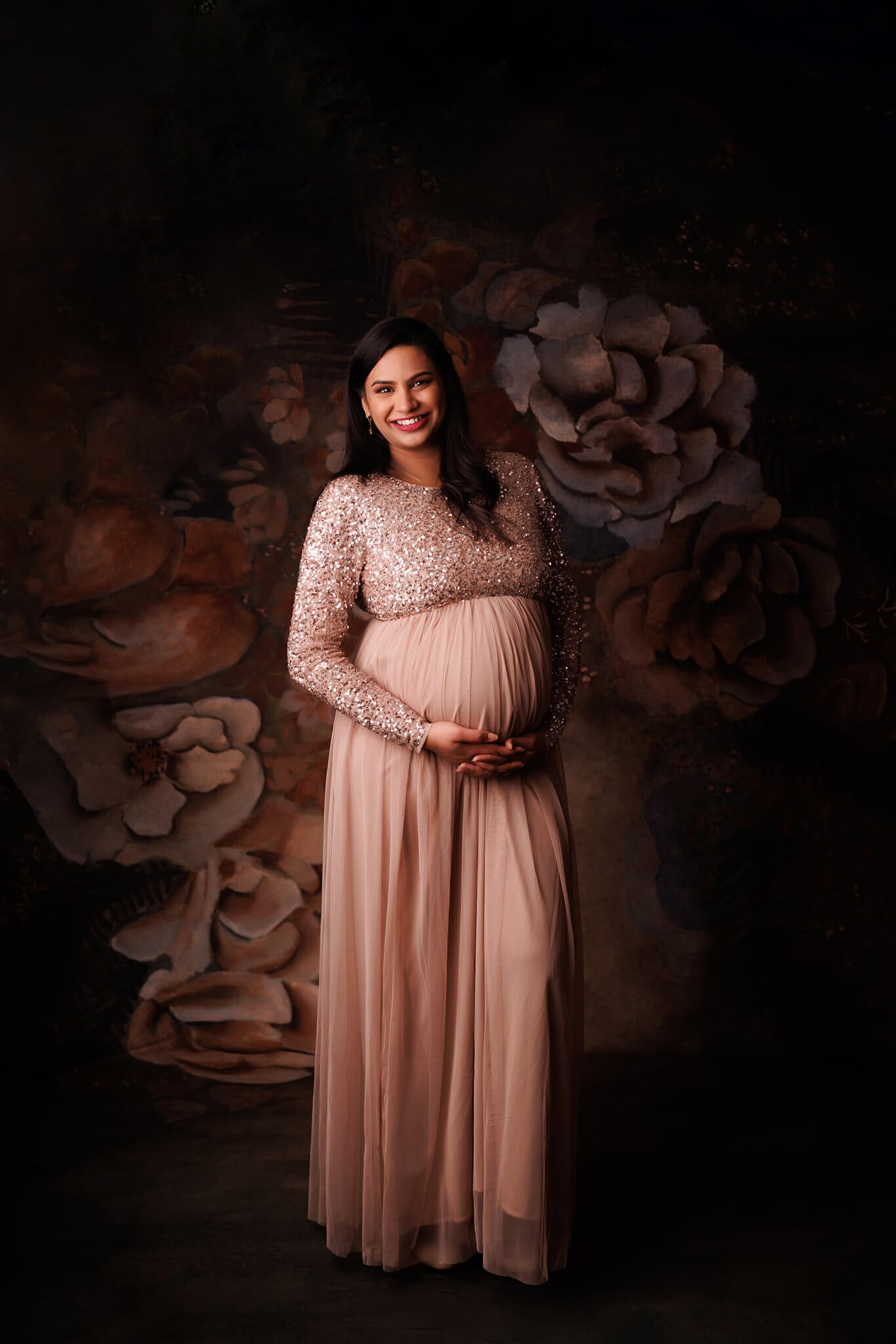 Pregnant woman smiling at the camera in a blush maternity gown with sequins