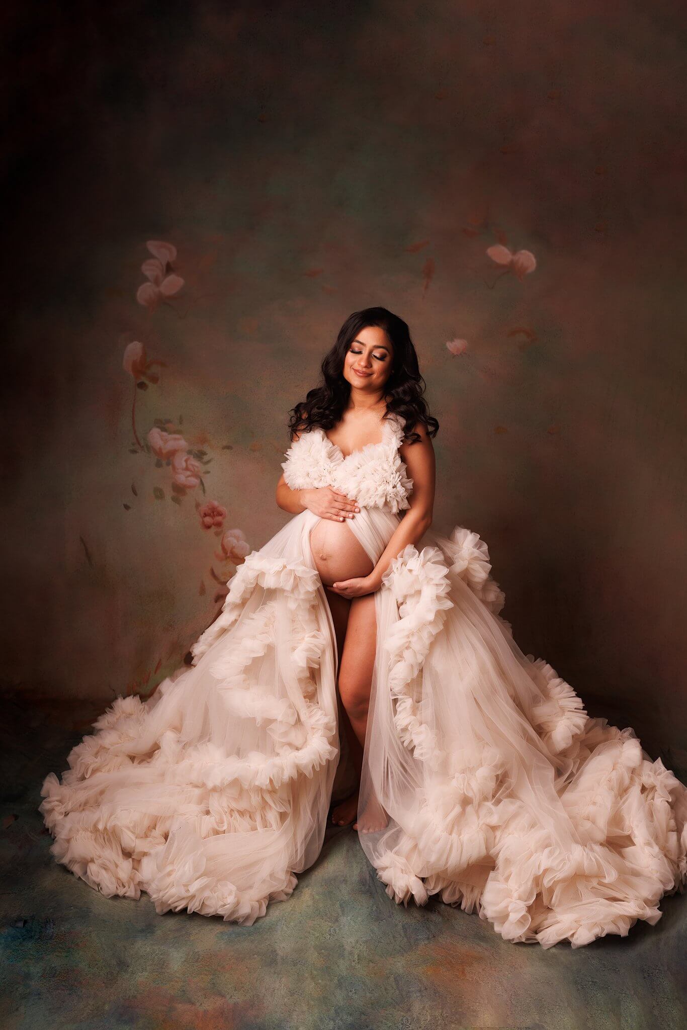 Woman in cream tulle gown with a floral backdrop holding pregnant belly Toronto Maternity Photographer Shanna Parker