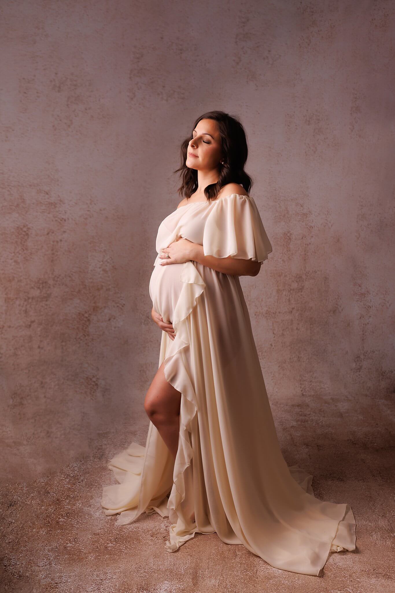 Pregnant woman in an ivory dress on a light backdrop