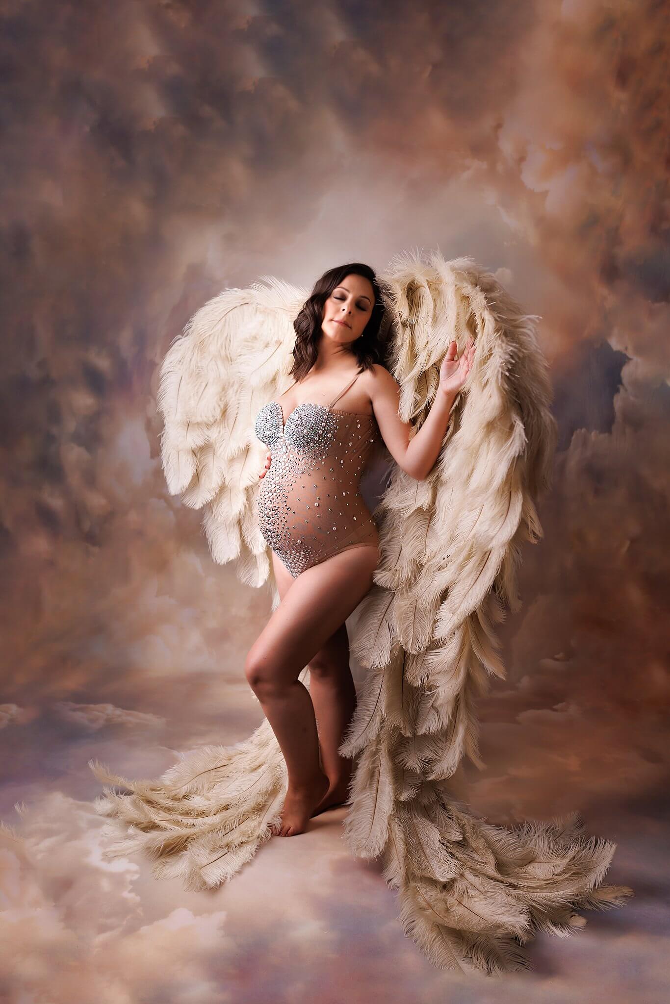 Pregnant woman modeling angel wings on a cloud backdrop