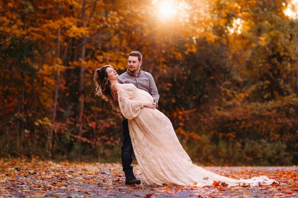 husband dips his pregnant wife in a park surrounded by fall colors and leaves Toronto Midwives