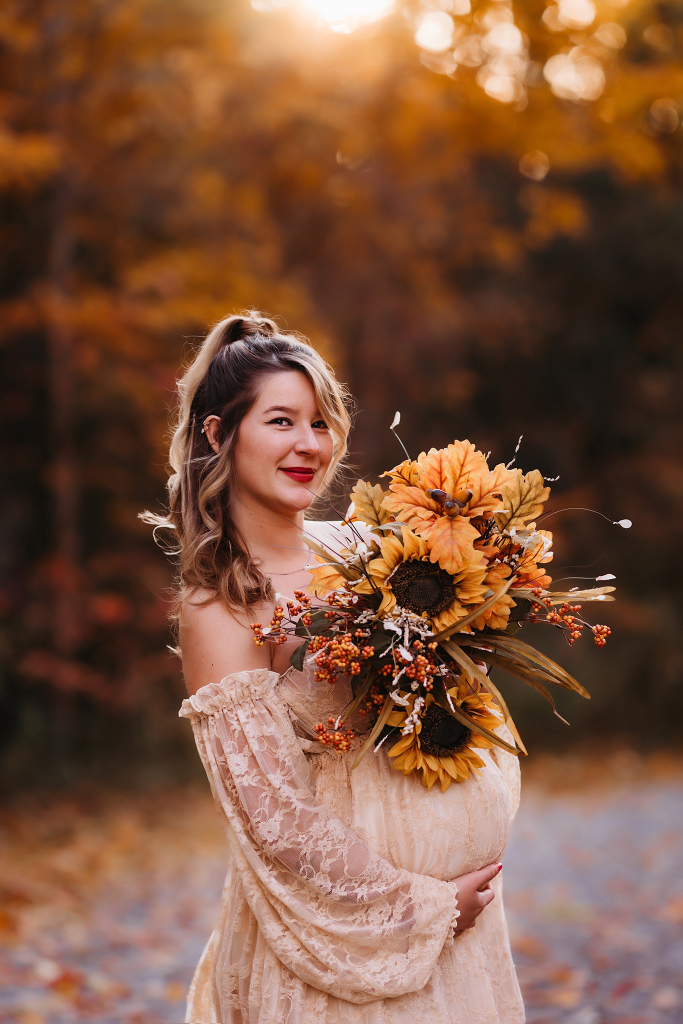 Mother to be in a lace maternity gown stands in a park holding large bouquet of sunflowers Toronto Midwives