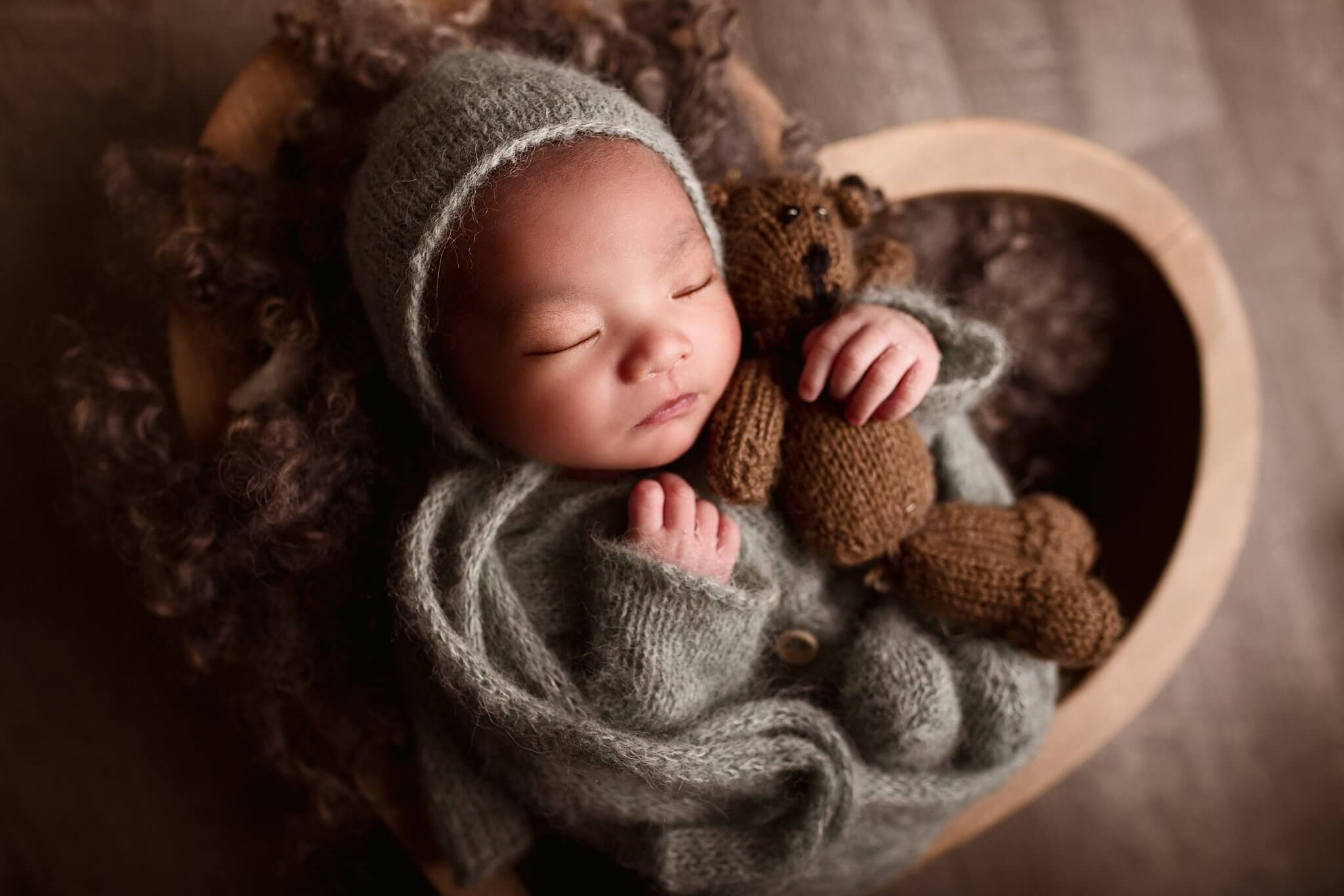 Adorable Newborn boy in a sage knit outfit with matching hat holding a small teddy bear by Toronto newborn Photographer