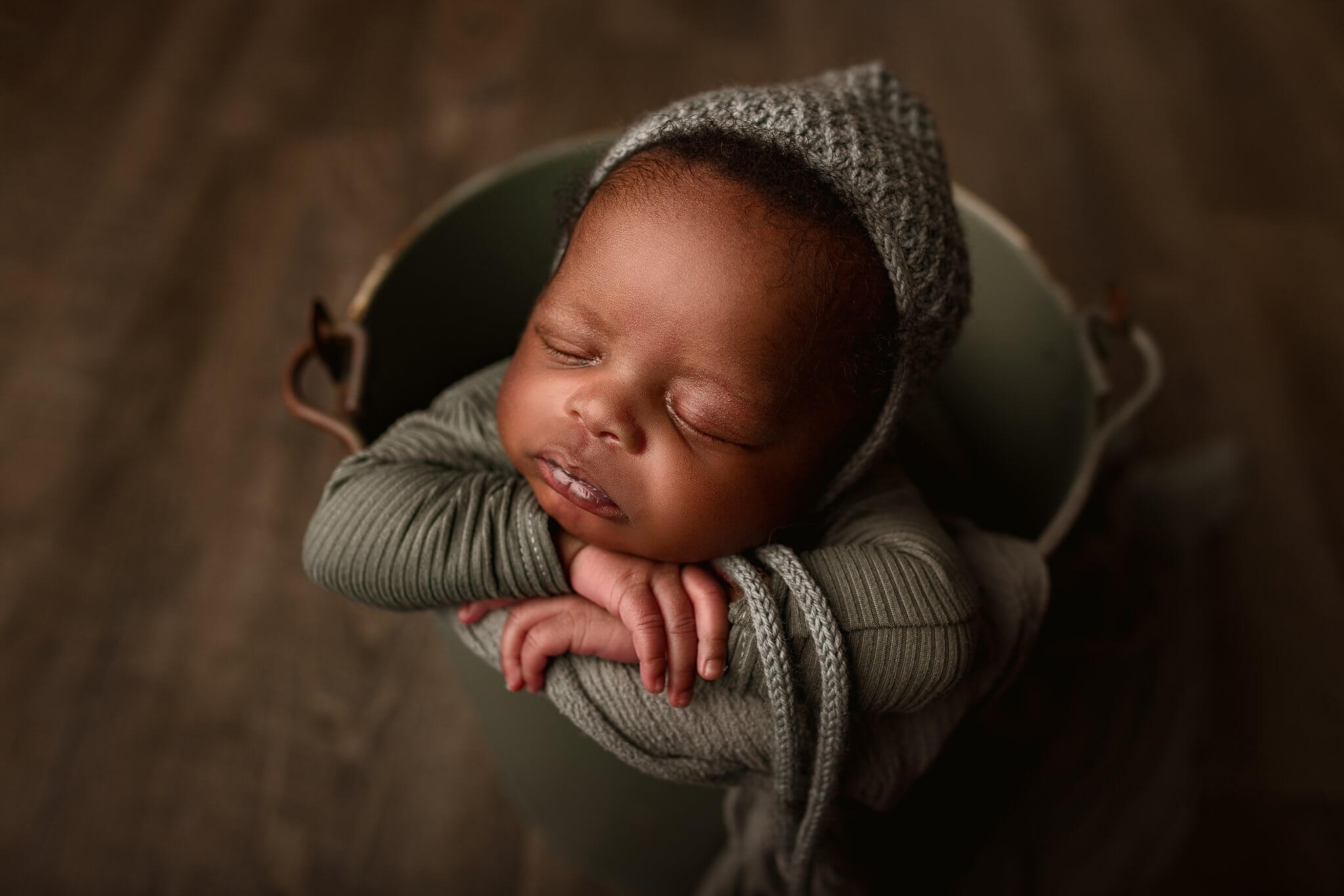 Newborn baby bow in a sage bucket, wearing a sage bonnet by Toronto Newborn Photographer