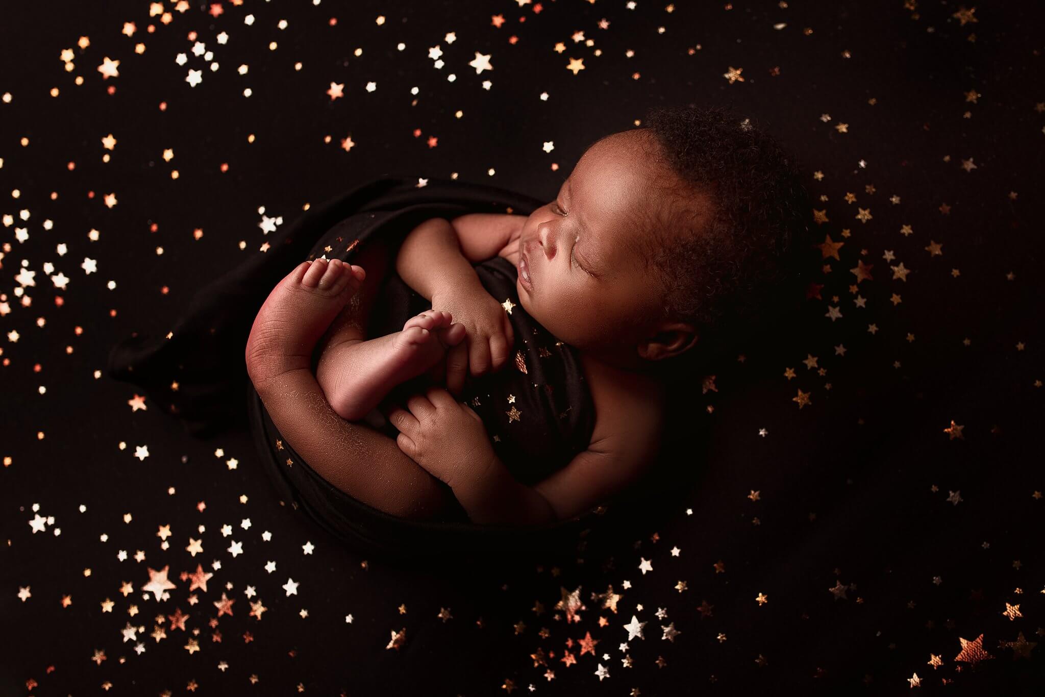 Newborn boy laying on a black backdrop with gold stars