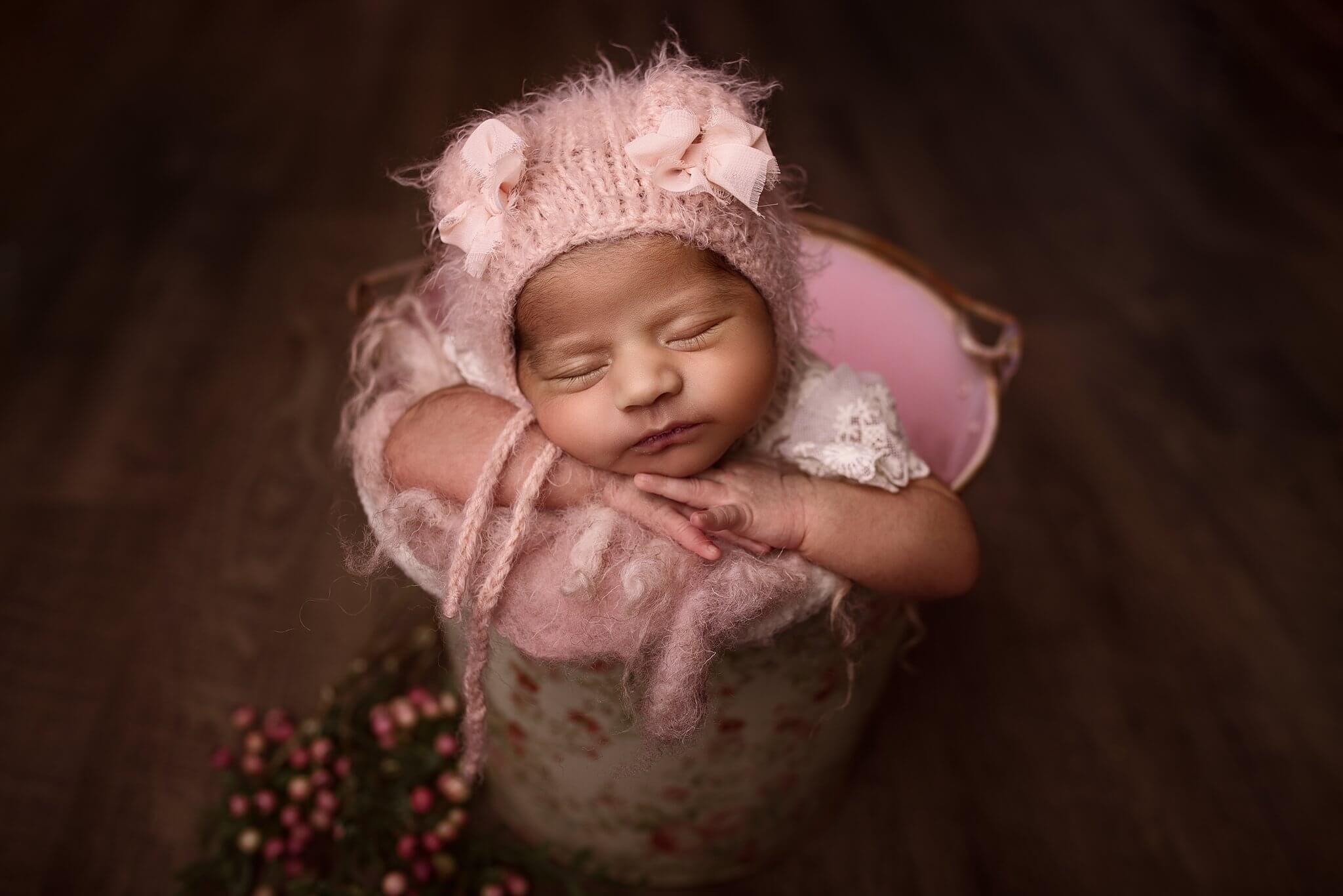 Toronto newborn photography photo of a newborn girl in a floral bucket wearing a pink teddy hat
