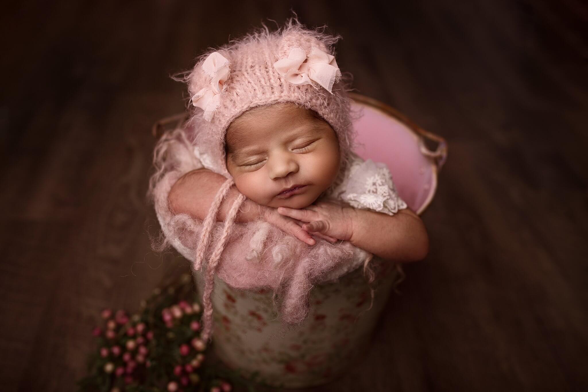 Photo of a newborn girl in a floral bucket wearing a pink teddy hat