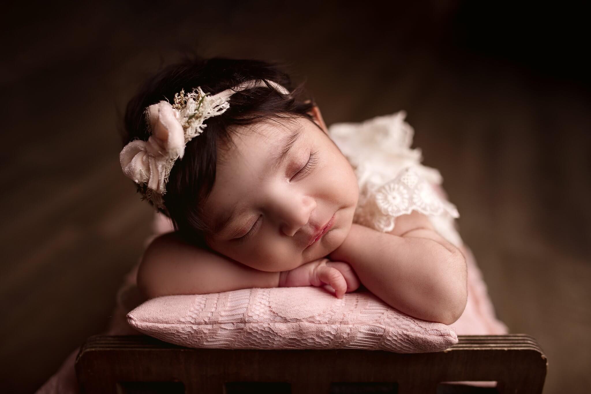 Newborn baby girl with her head on her hands on a pink pillow, sleeping and facing the camera