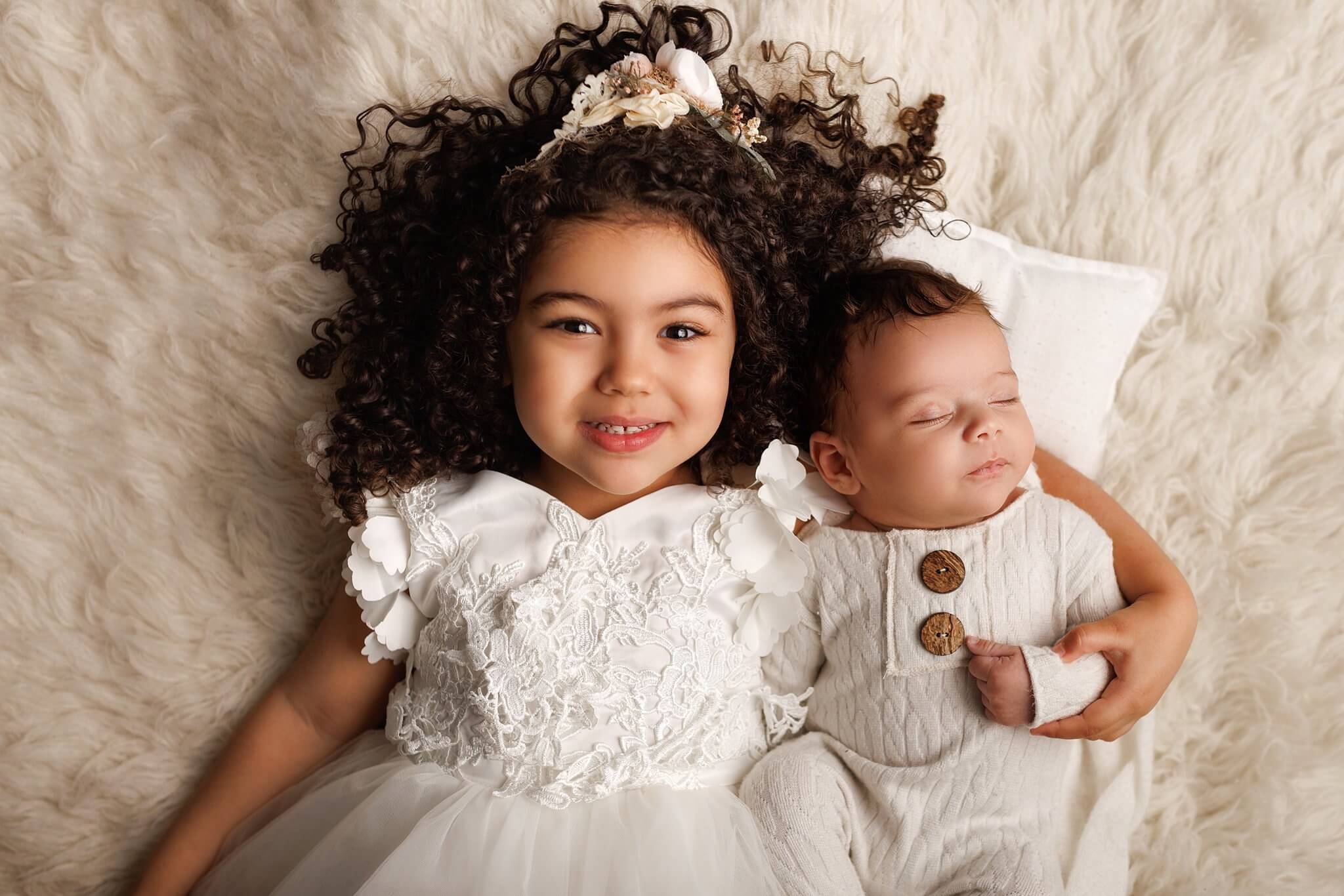 Siblings, Newborn boy with his older sister who is in a white dress. Both are laying on white fur
