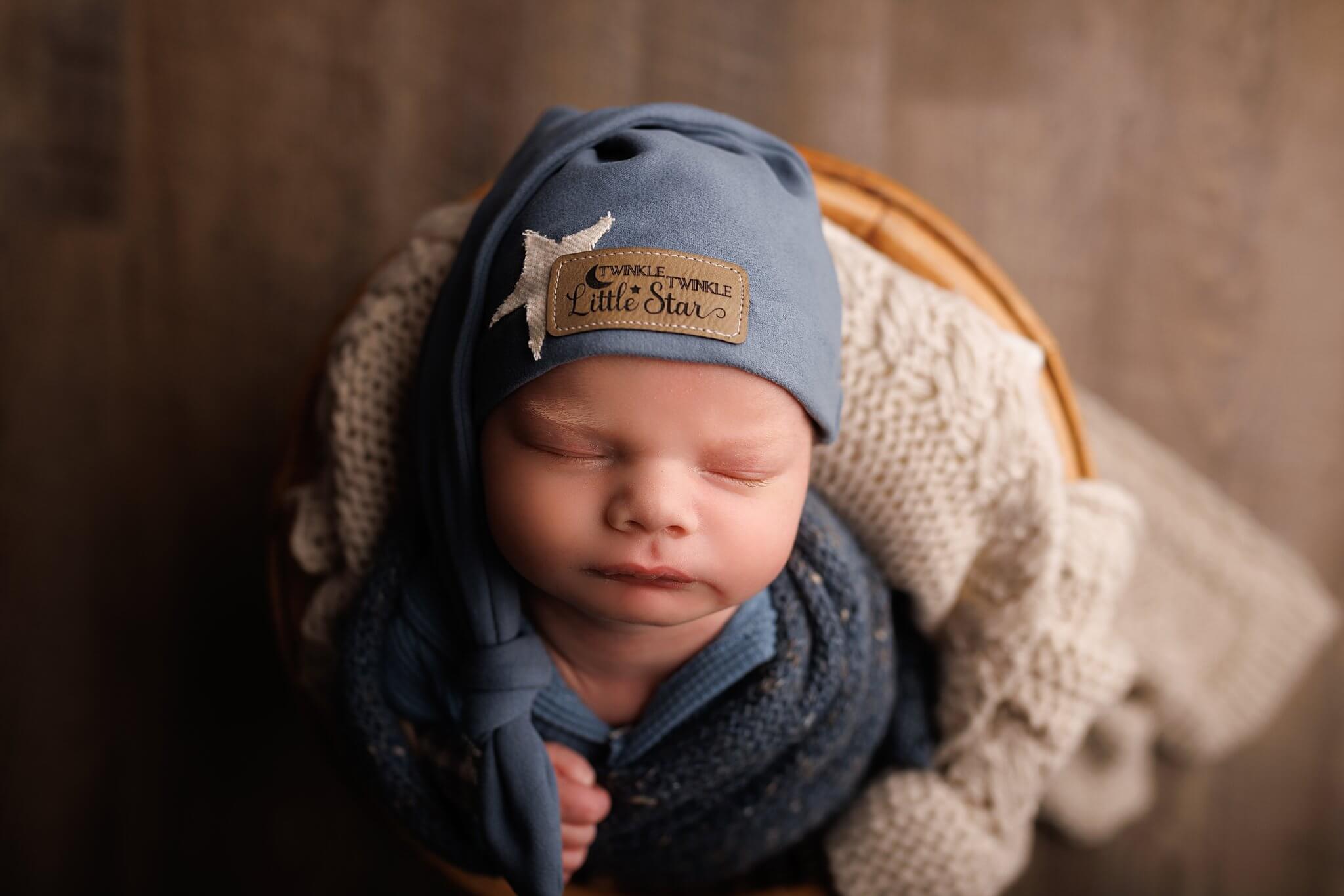 baby boy in a blue wrap with a Twinkle Twinkly sleepy cap on