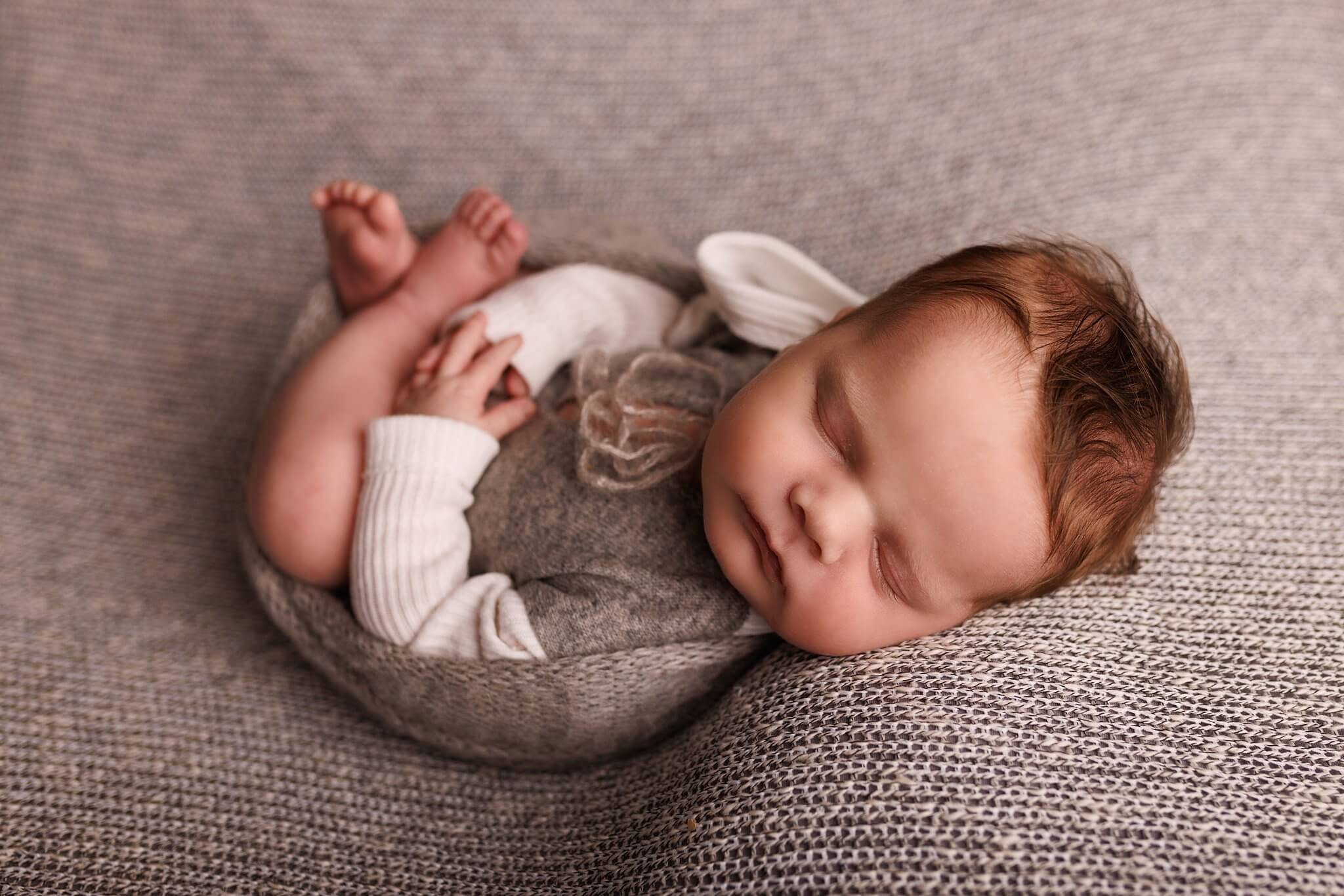 Newborn boy on a grey textured backdrop in a cute hooded outfit