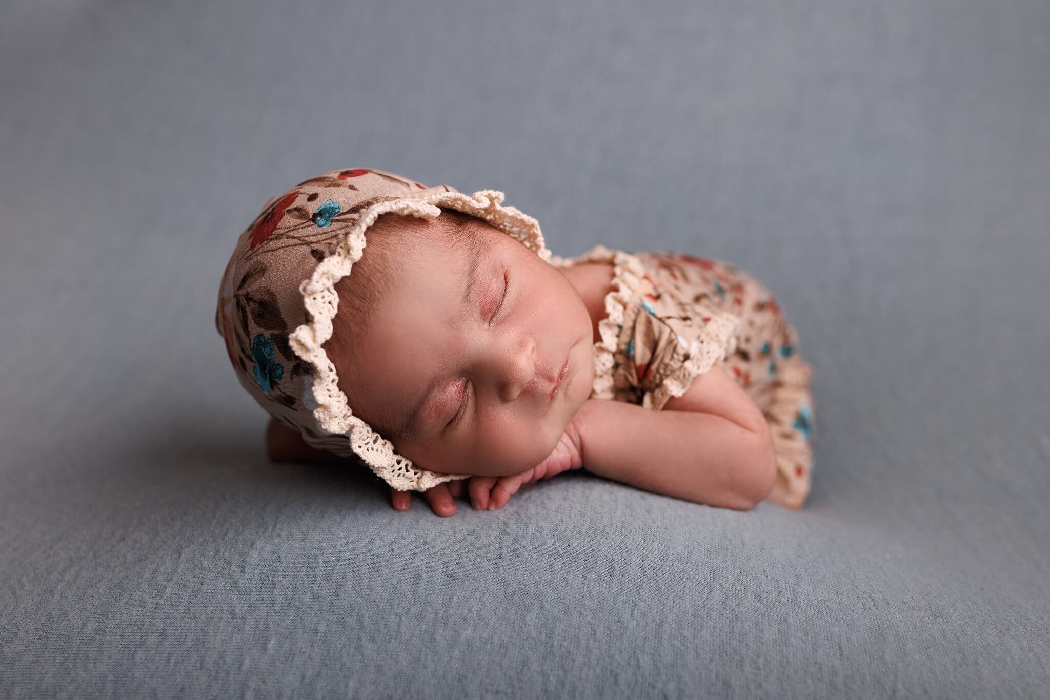 Newborn baby girl on a blue backdrop in a floral print bonnet and outfit