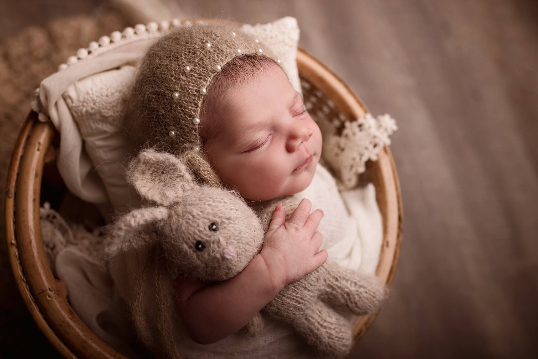 Newborn Baby girl in a bonnet with pearls holding a stuffed bunny