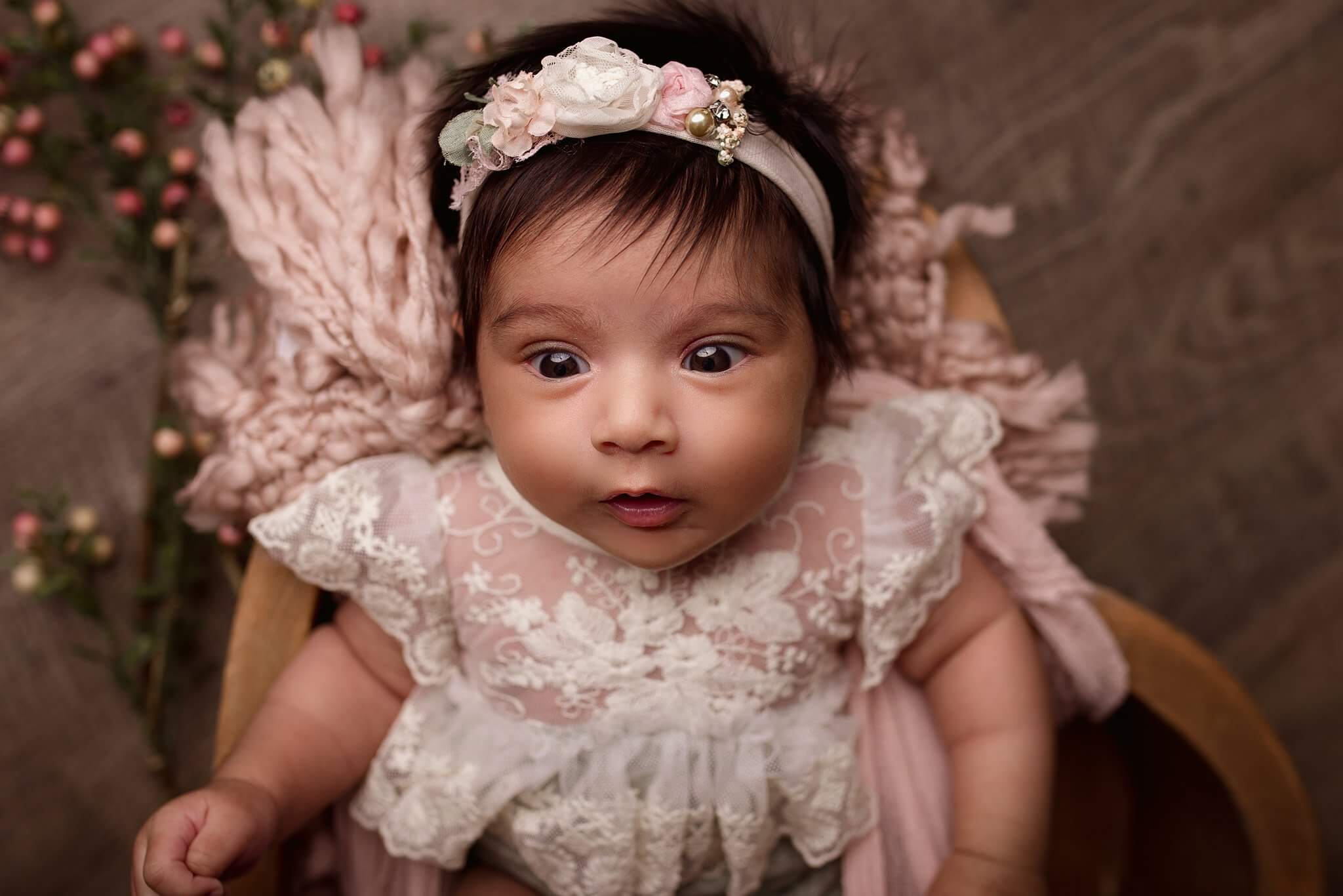 Bright eyed baby girl in a lace outfit on a pink blanket