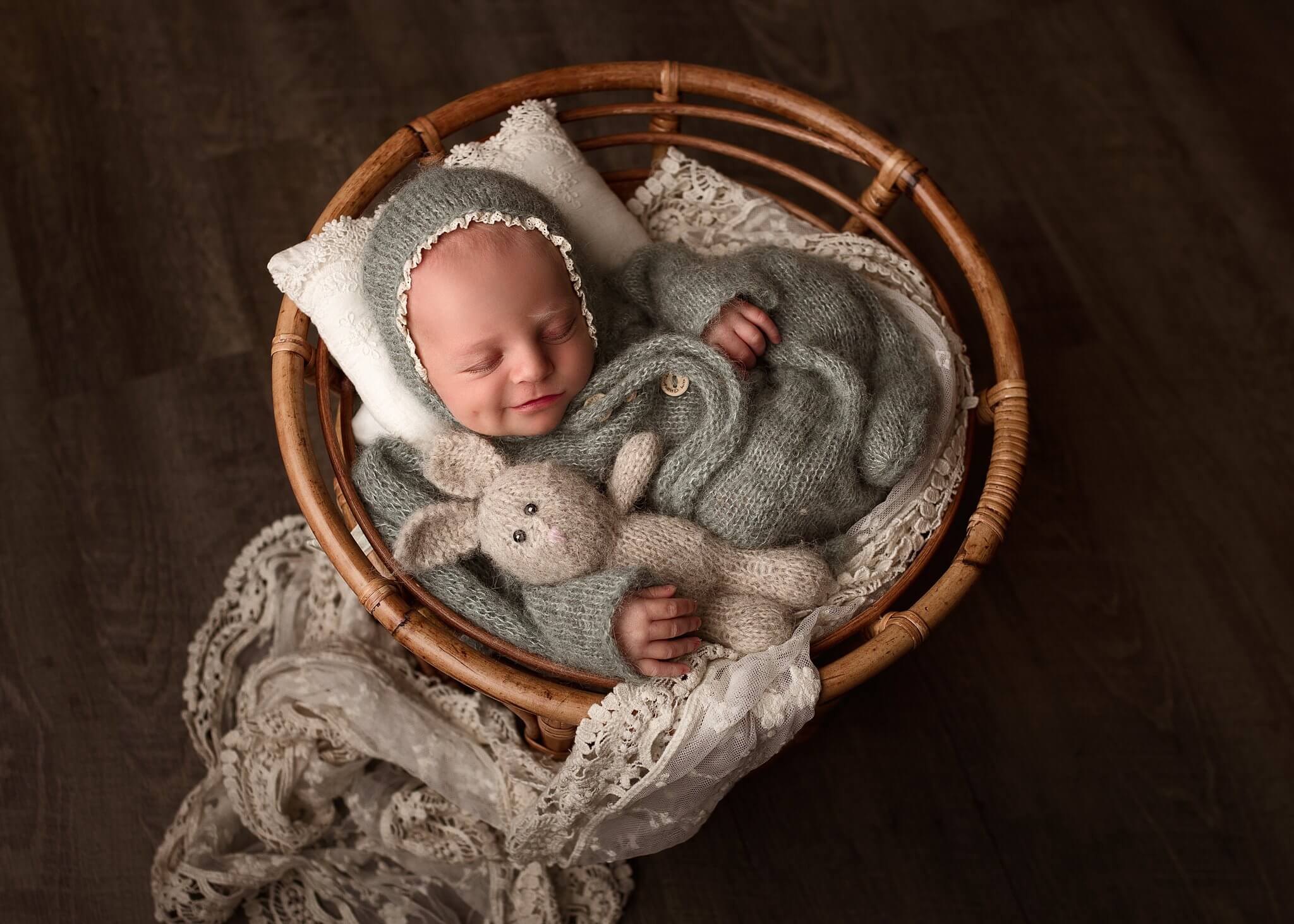 Newborn baby girl in sage outfit holding a small bunny in a round bamboo basket