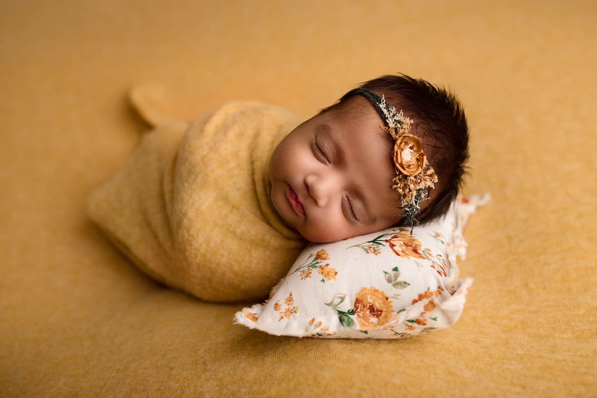 Newborn Baby Girl on Mustard fabric with a floral headband on a floral pillow