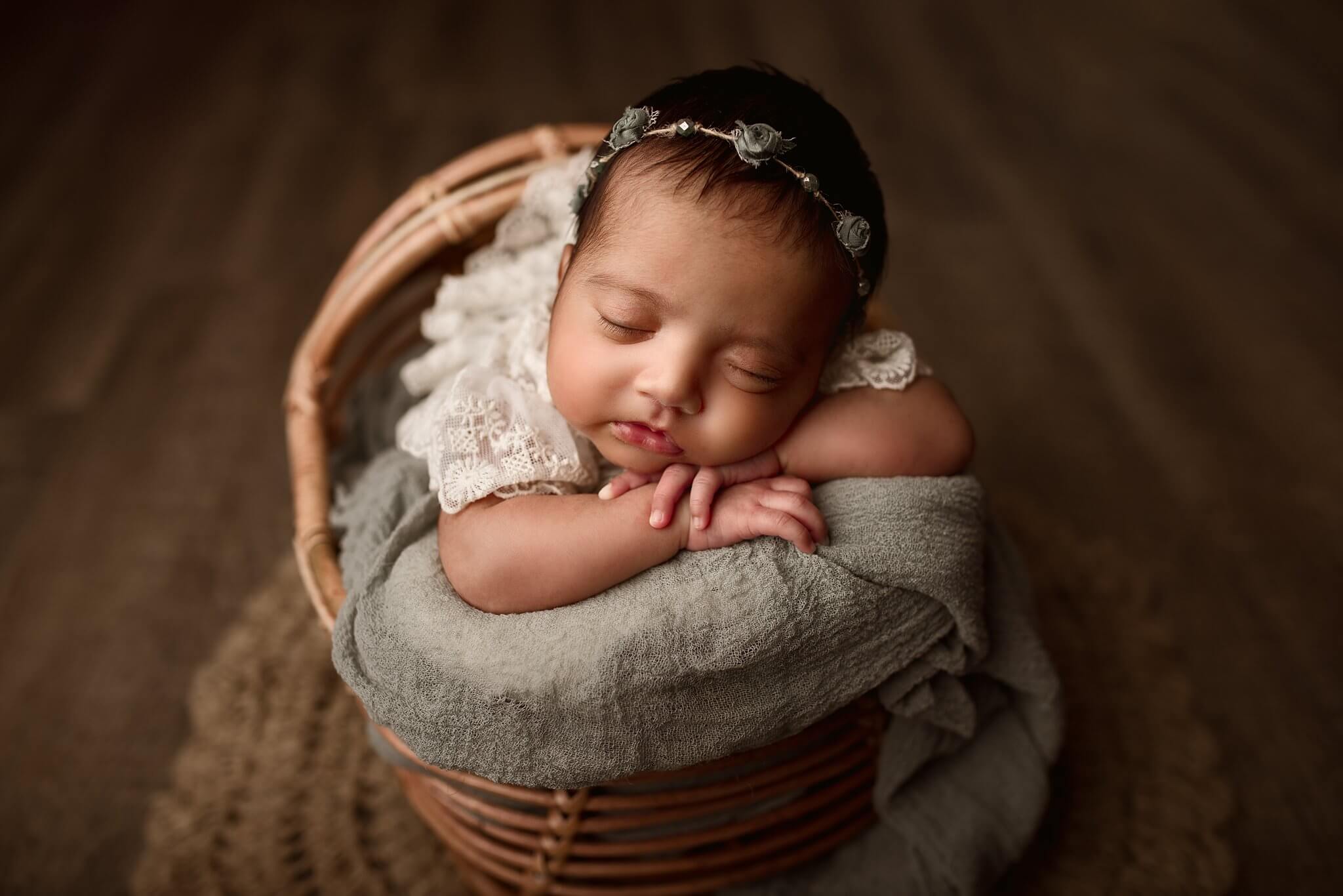 Baby girl in a lace outfit on a sage pillow in a basket