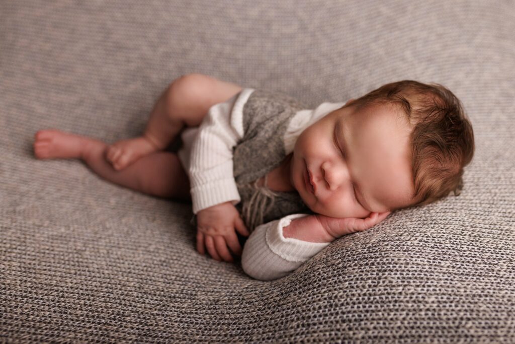 A newborn baby sleeps with head resting on hand in a grey with white sleeves shirt