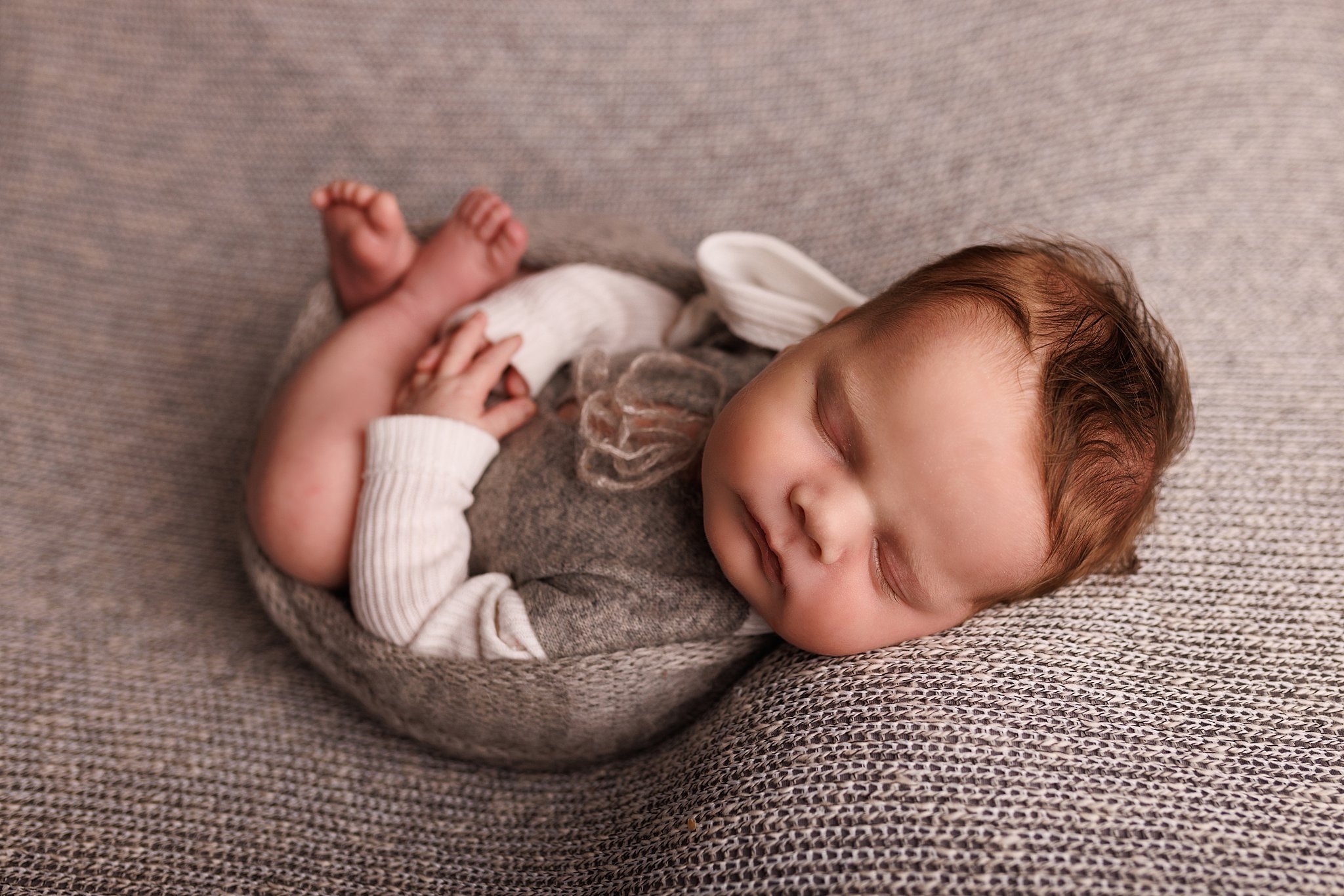 A newborn baby boy wearing a grey and white sweater sleeps on a grey blanket Toronto baby clothes