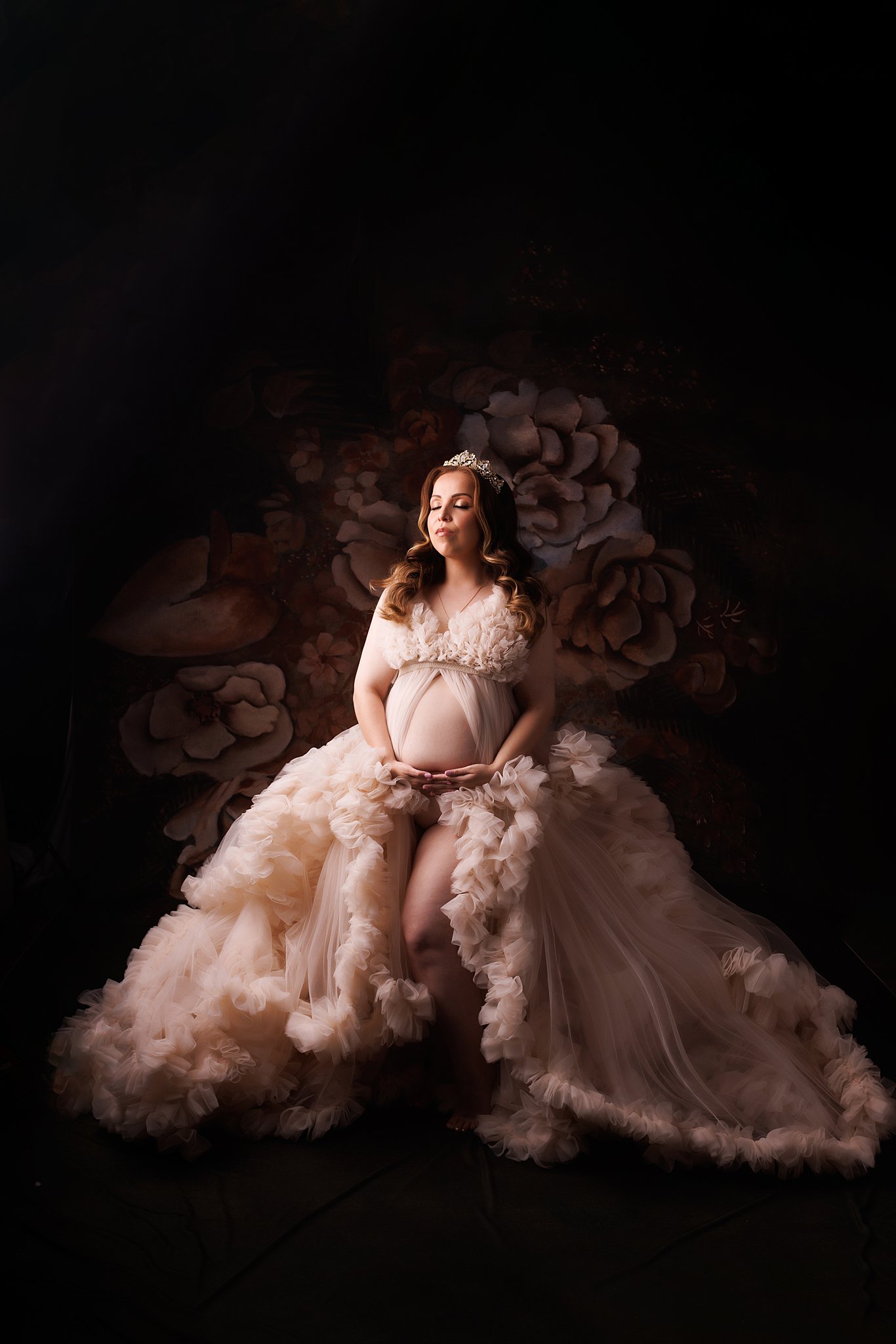 mother-to-be stands in a studio wearing a large flowing tule maternity gown Toronto prenatal massage