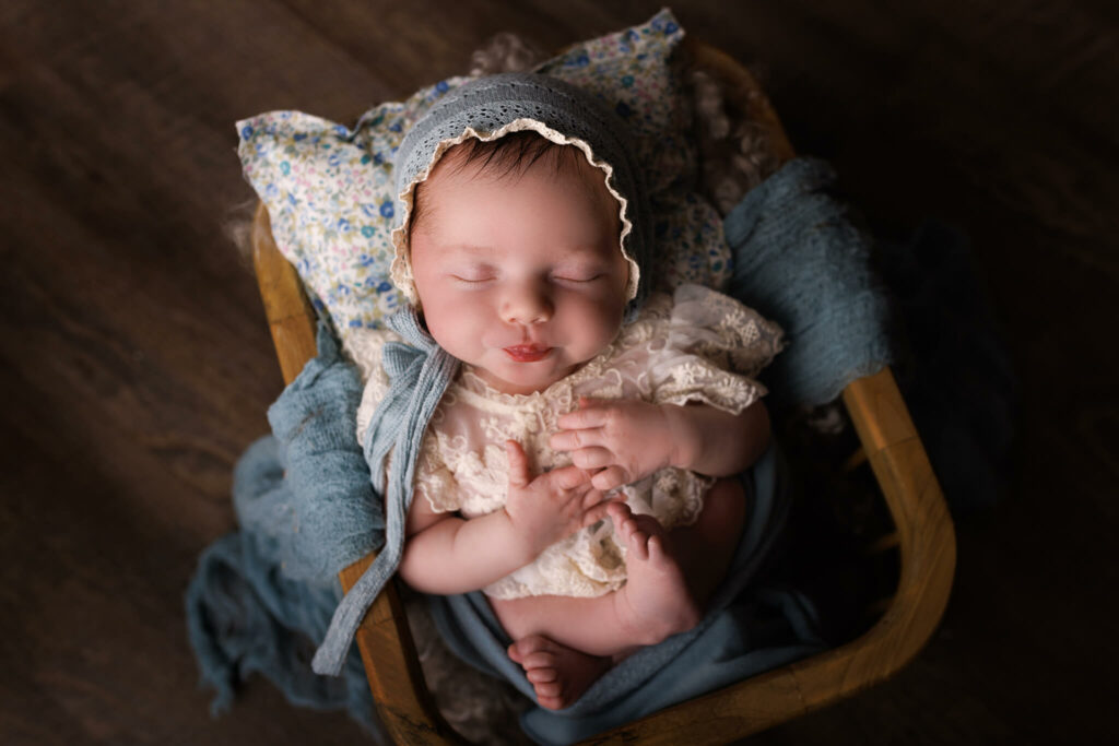 A newborn baby sleeps in a lace dress and blue bonnet