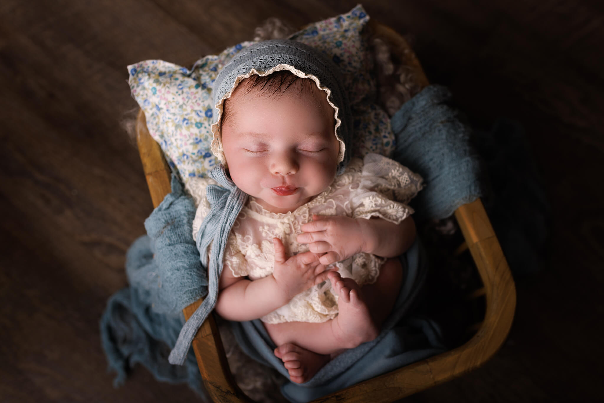 A newborn baby sleeps in a lace dress and blue bonnet