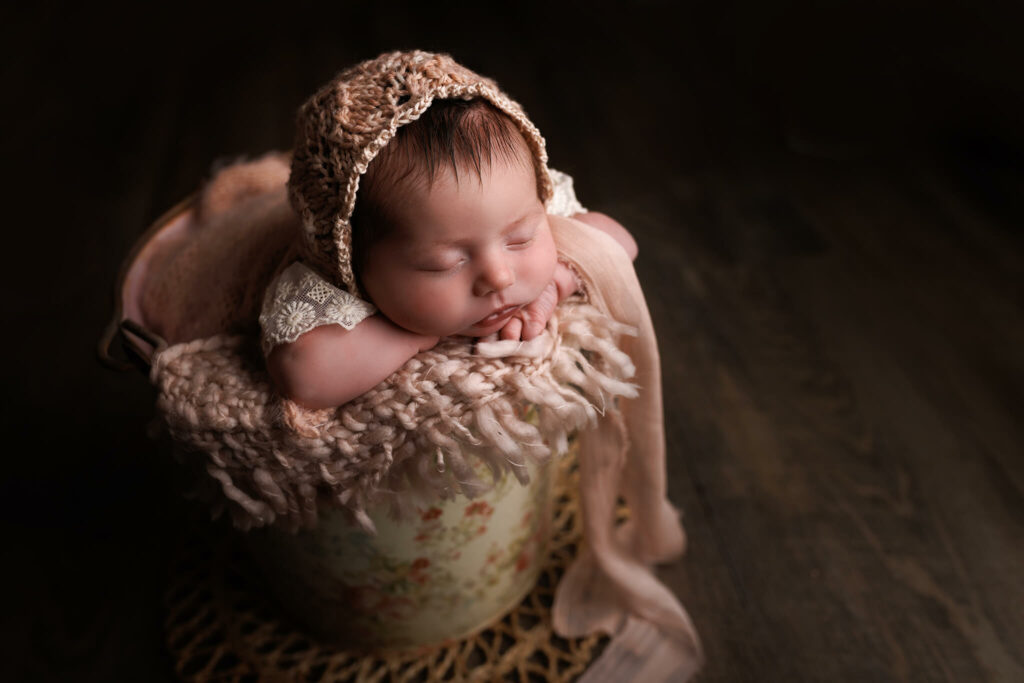 A newborn baby sleeps in a bucket resting herr head on her hands advice from a caterpillar