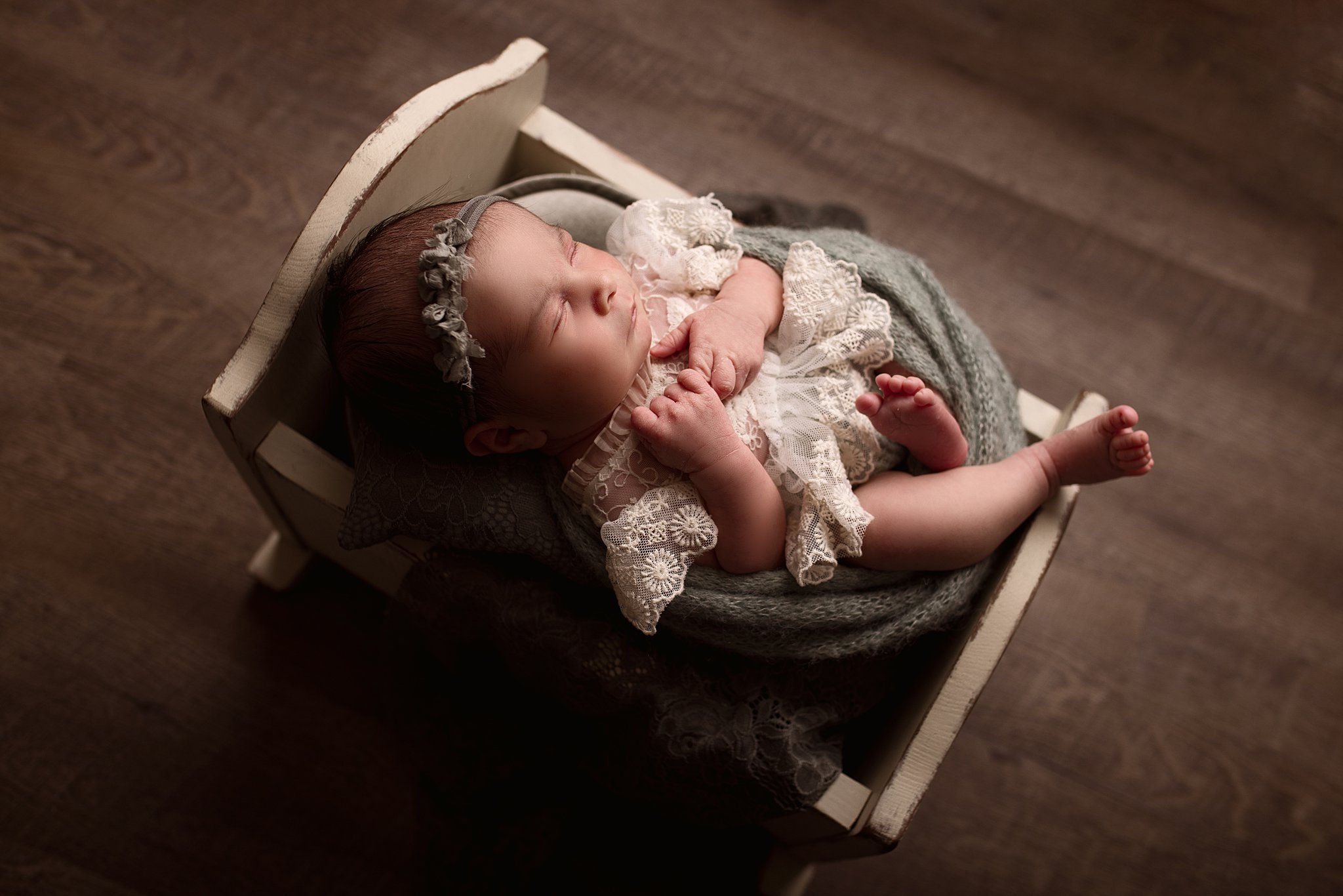 newborn sleeps in a white lace dress in a tiny wooden crib baby furniture toronto