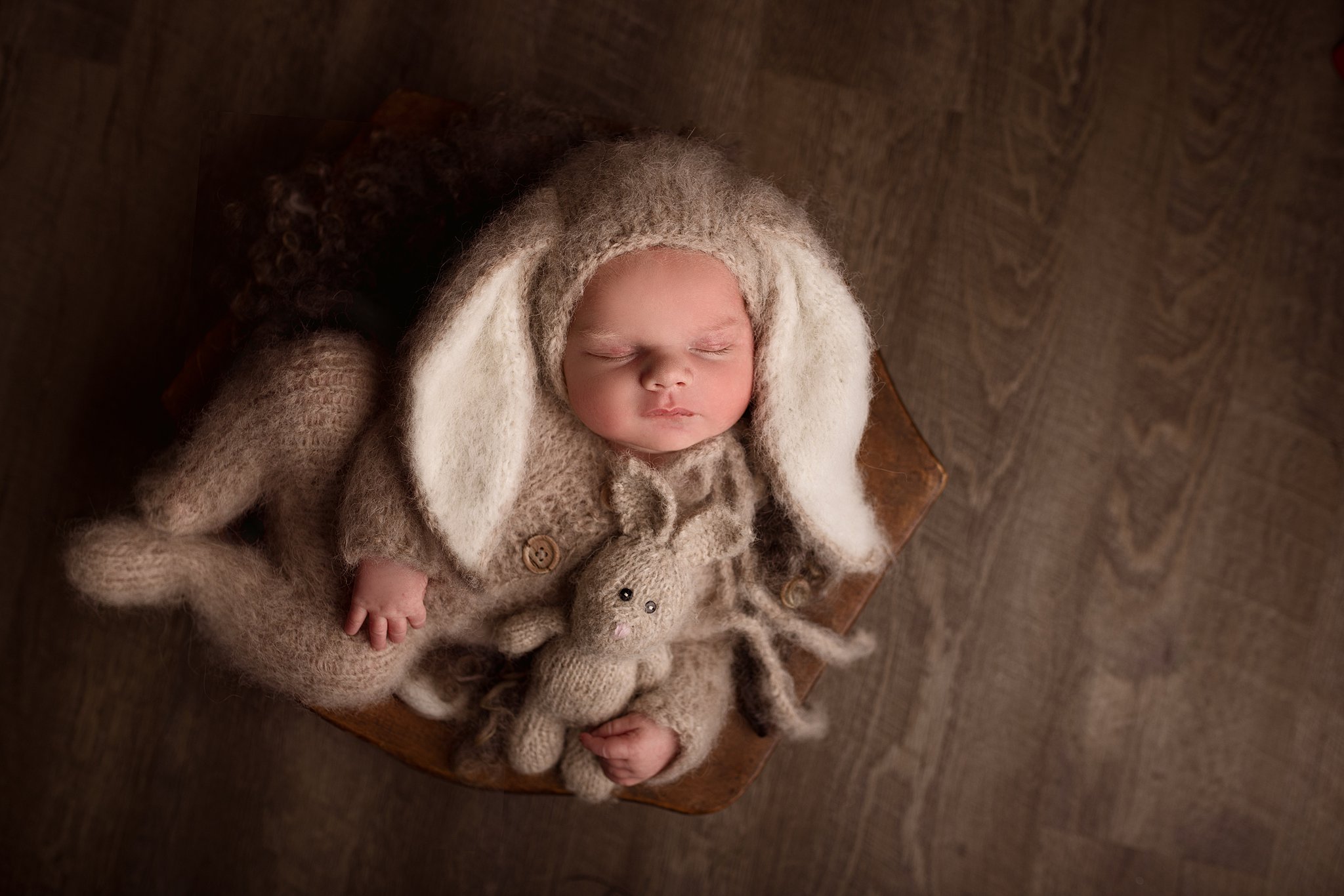A newborn baby in a knit bunny costume with large ears sleeps on a bench on dark wood flooring baby furniture vaughan